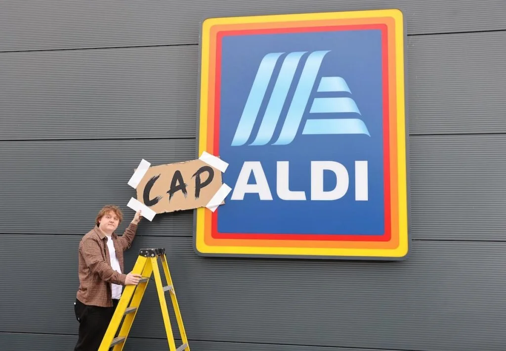 Lewis Capaldi holding a cardboard sign up of 'Cap' to Aldi for a recent campaign.