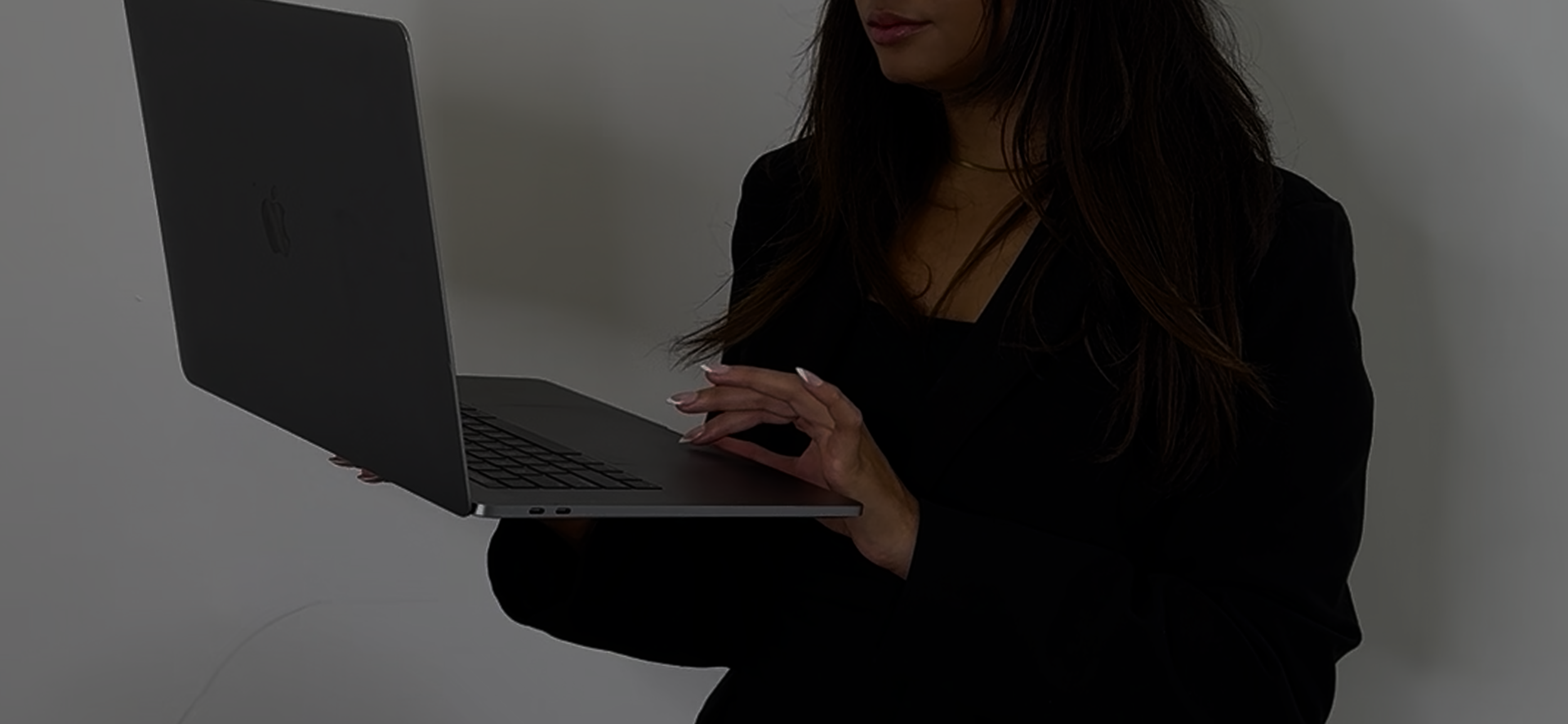 A low exposure photo of a woman scrolling on her laptop.