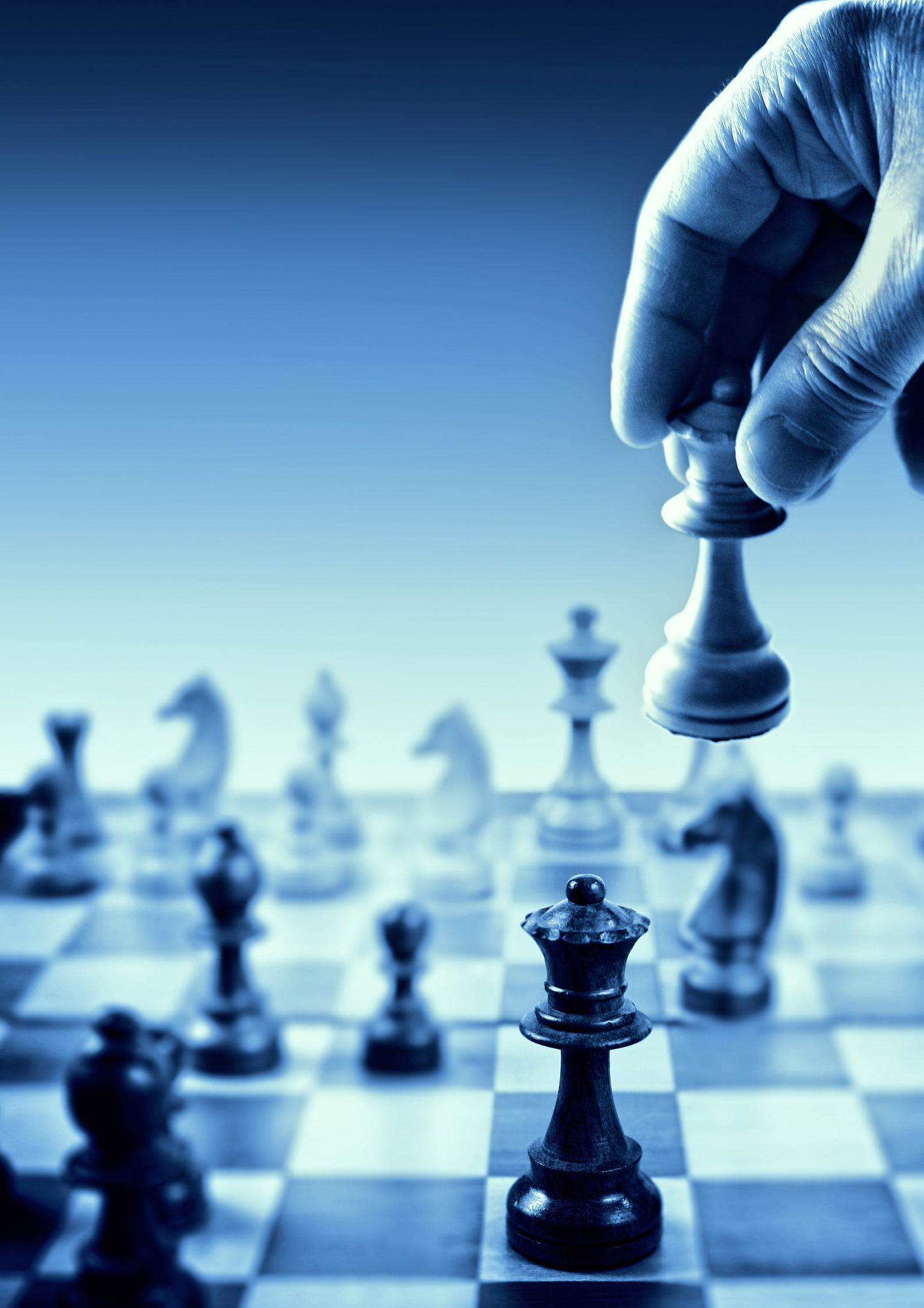 Close-up of a hand moving a white king chess piece on a chessboard, with other chess pieces in the background.