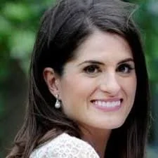 Smiling woman with long dark hair wearing white earrings, set against a blurred green background.