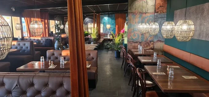 Interiör av en restaurang med bruna lädersoffor, träbord, hängande lampor och dekorationer på väggen. Flera bord har vattenflaskor och bestick redo för gäster.