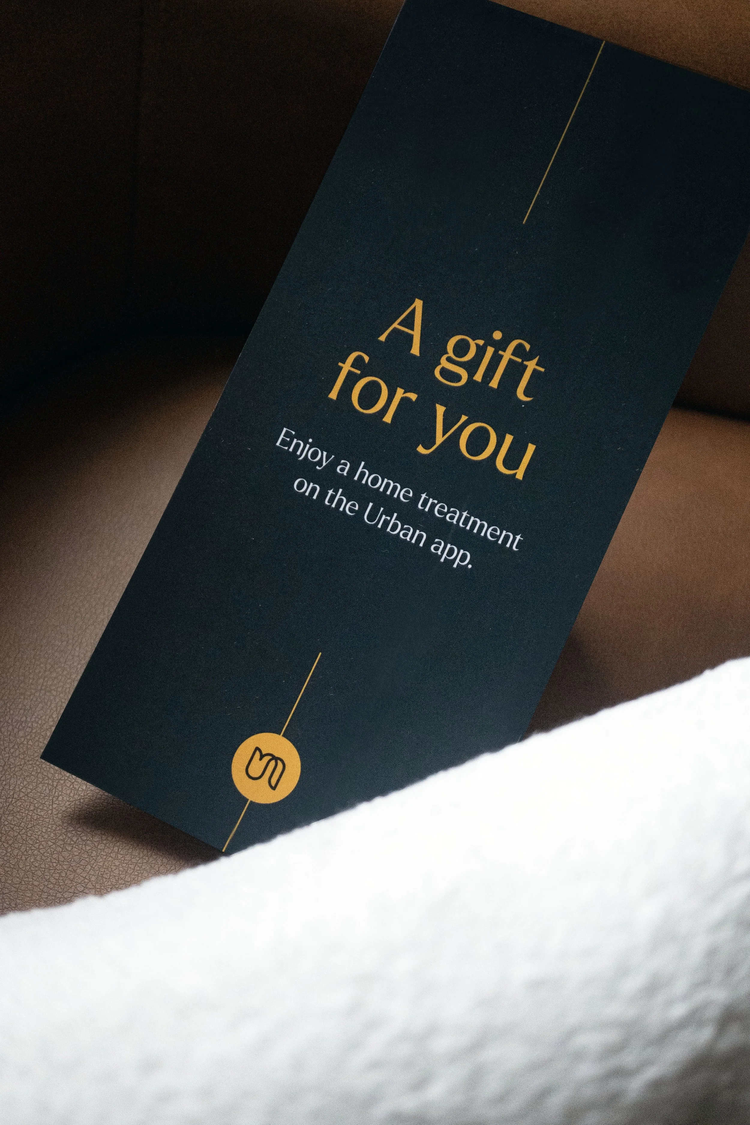 A dark blue card with gold text that says 'A gift for you. Enjoy a home treatment on the Urban app' with a gold icon of a hand pointing at a button at the bottom.