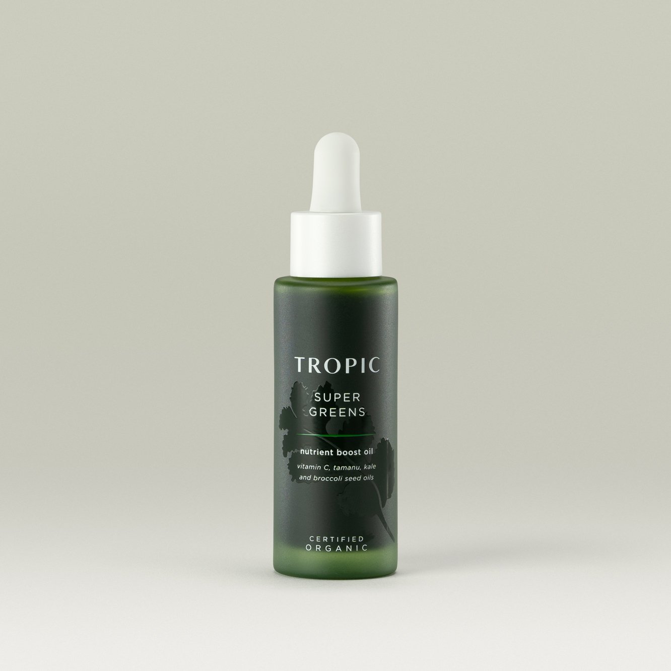 A green bottle of Tropic Super Greens nutrient boost oil with a white dropper cap, labeled with ingredients like vitamin C, tamanu, kale, and broccoli seed oils, against a neutral background.