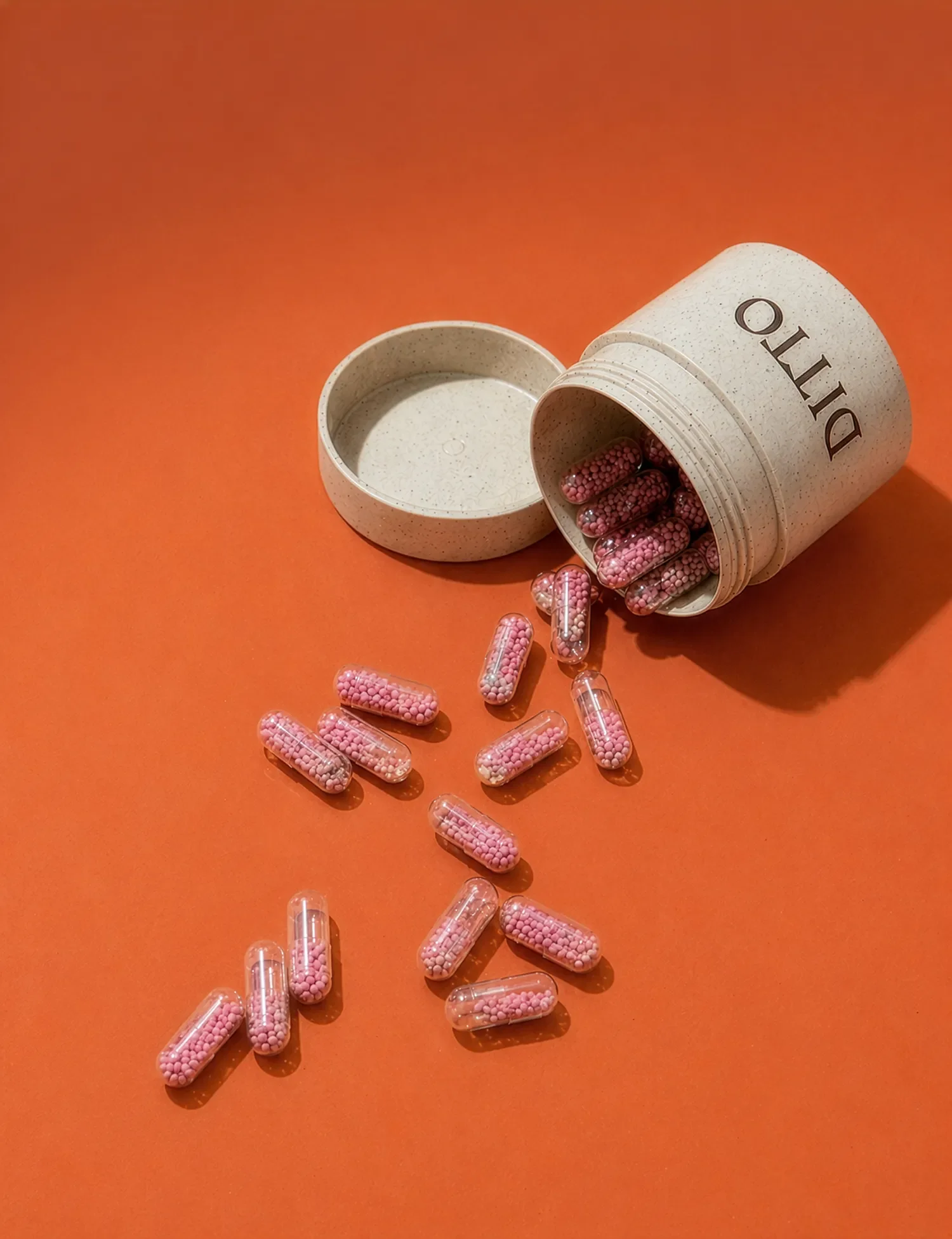 An open pill bottle labeled "DITO" with pink capsules spilling onto an orange surface.