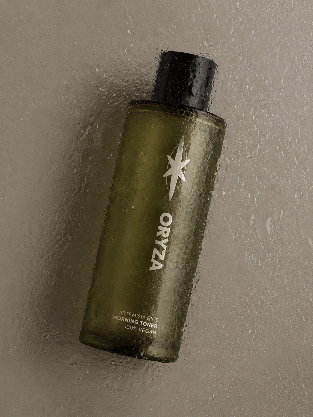 A green bottle of Oryza Artemisia Rice Morning Toner with a black cap, covered in water droplets, placed on a wet, foggy surface.