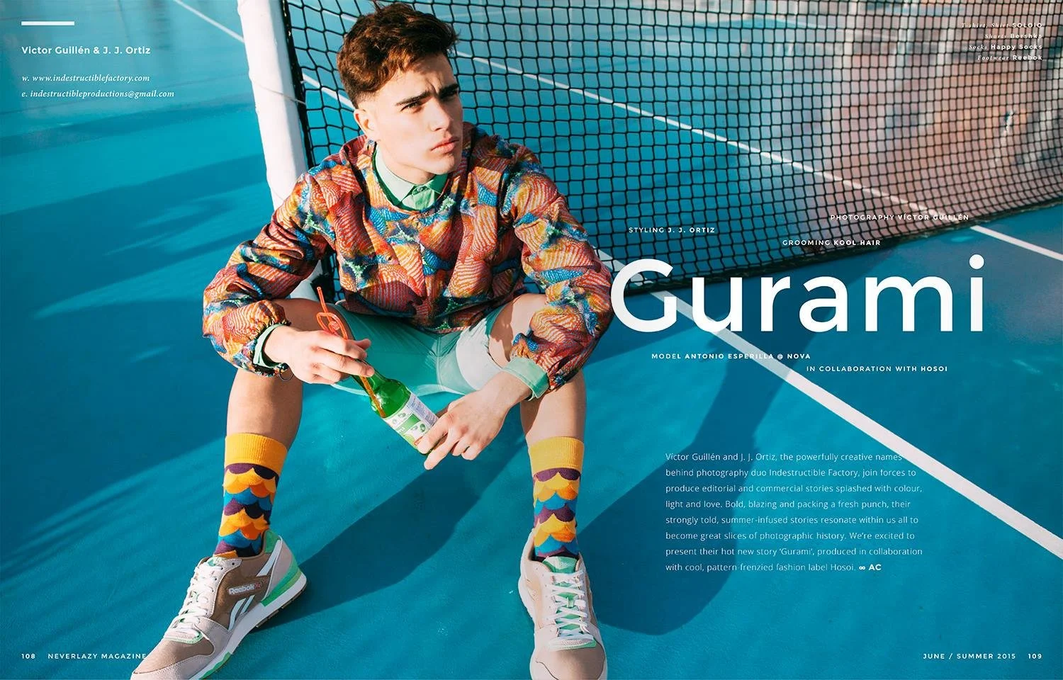 A young man sitting on a tennis court, holding a bottle, wearing colorful patterned socks, beige sneakers, and a patterned jacket. The background shows the net and blue court surface.
