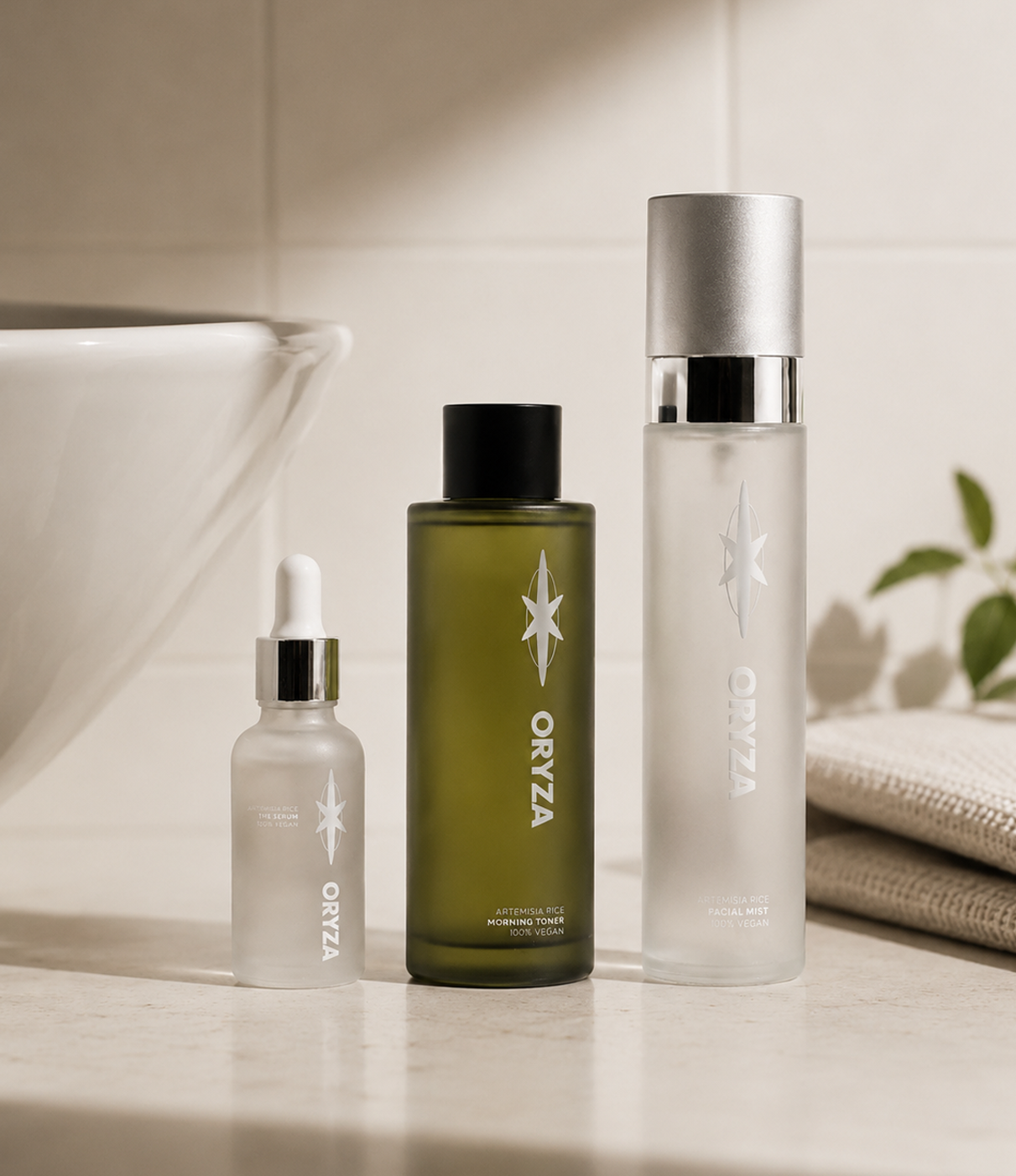 Three skincare bottles with the brand name Oryza on a bathroom counter, next to a folded towel and a plant in the background.