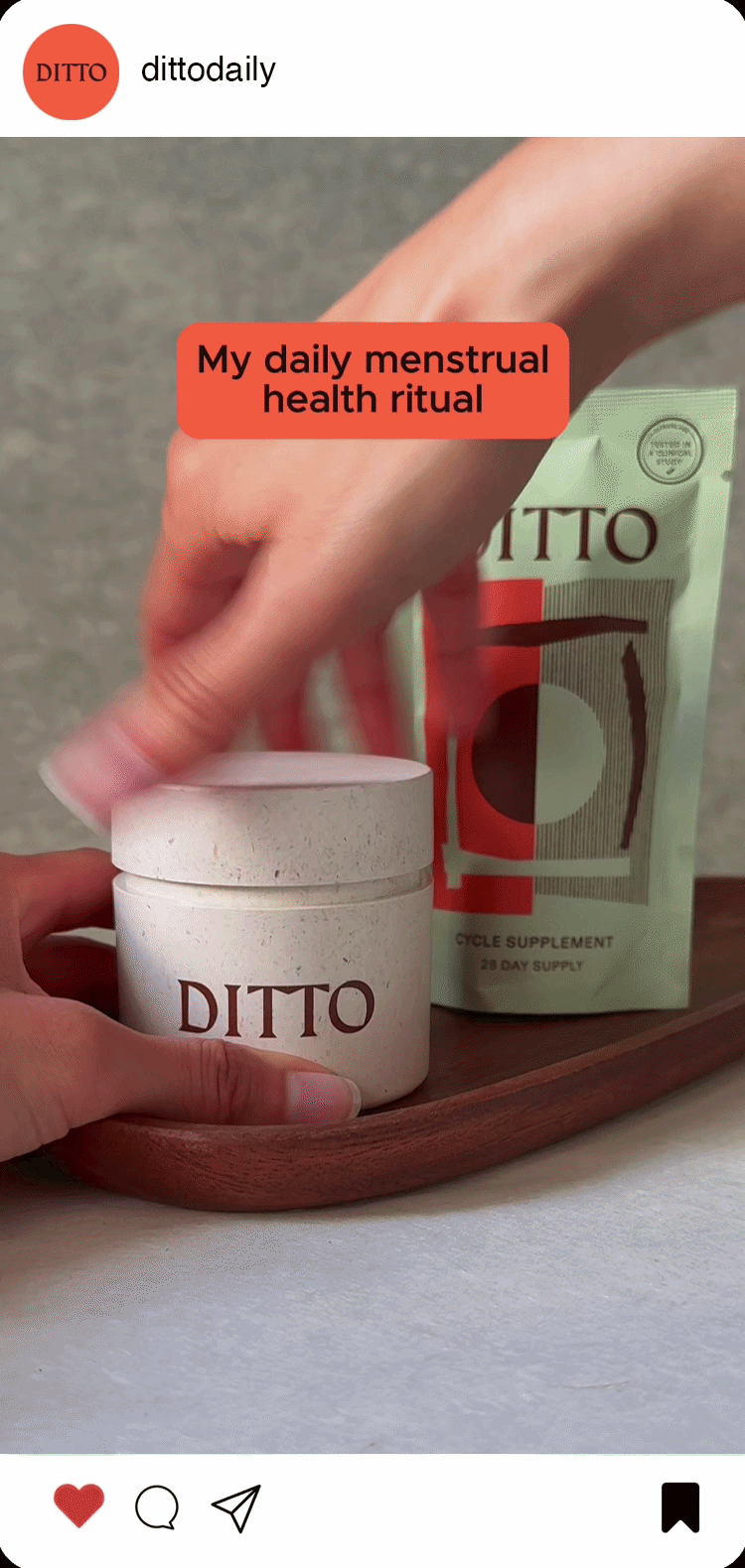 A person holding a white container labeled 'DITTO' with a pouch of 'DITTO' cycle supplement behind it, emphasizing a daily menstrual health ritual.