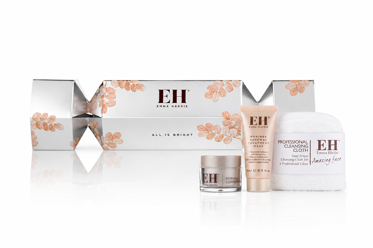 Emma Hardie skincare set including a large silver box with pink leaf design, a white cleansing cloth, a small jar labeled 'Moringa Cleansing Balm', a tube labeled 'Moringa Renewal Treatment Mask', and a white towel, all featuring the Emma Hardie logo.