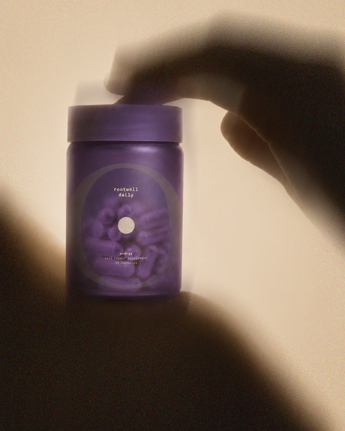 Purple bottle labeled "rootwell daily energy cell repair supplement 30 capsules" is being held by a person's hand against a neutral background.