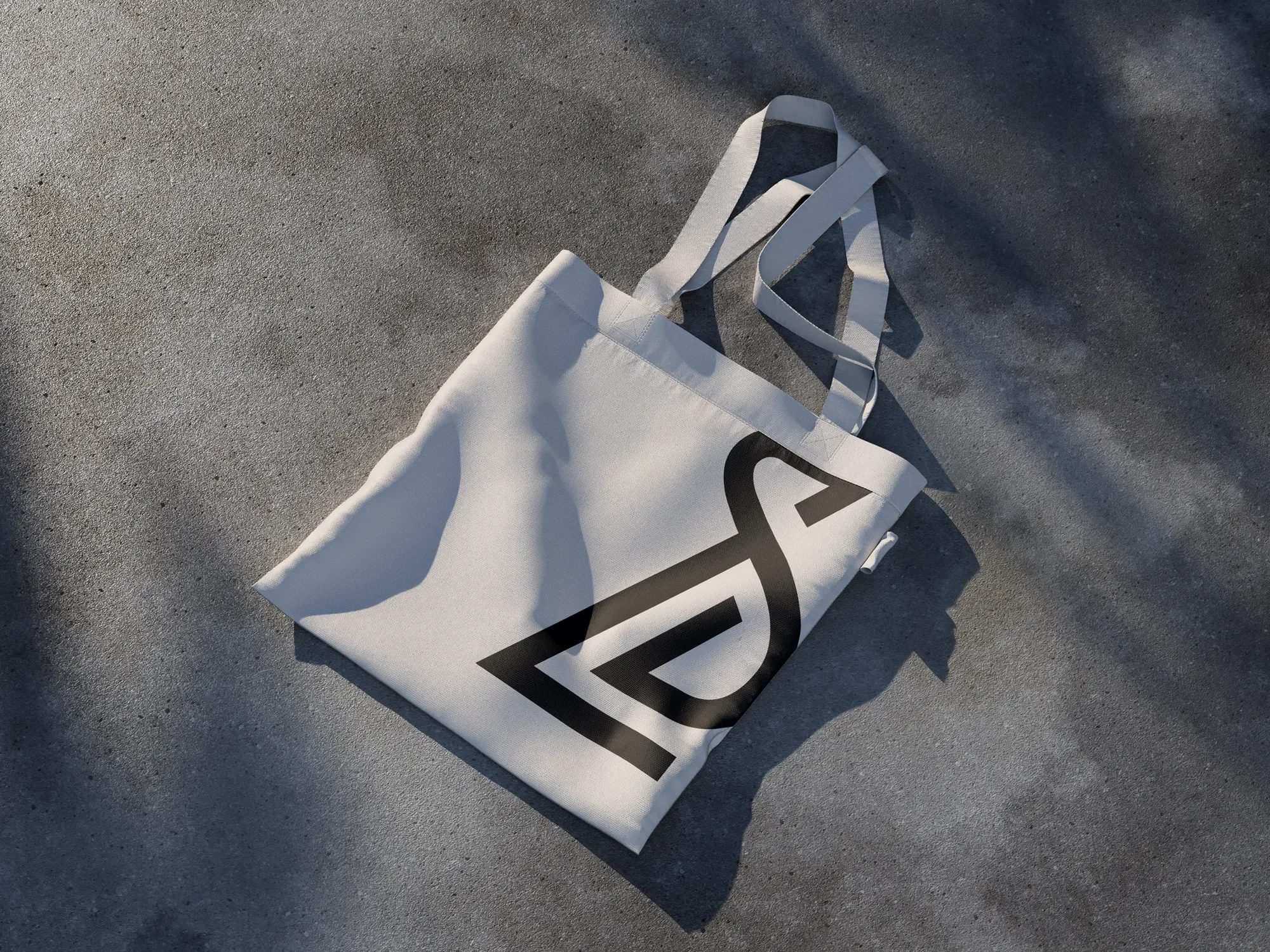 A white fabric shopping bag with black lettering lying on a gray concrete surface.