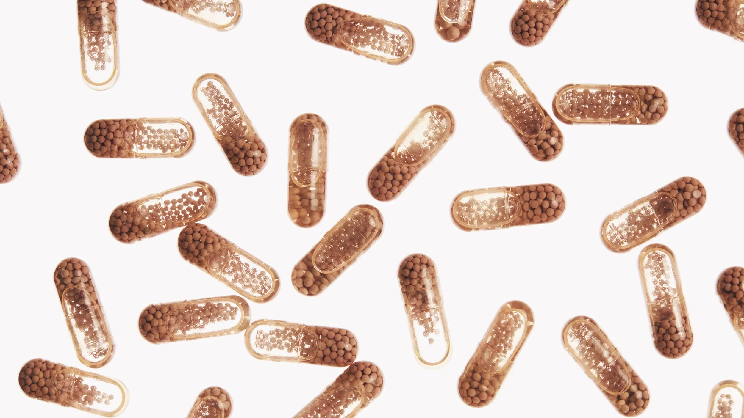 Multiple capsules containing small brown beads inside, scattered against a white background.