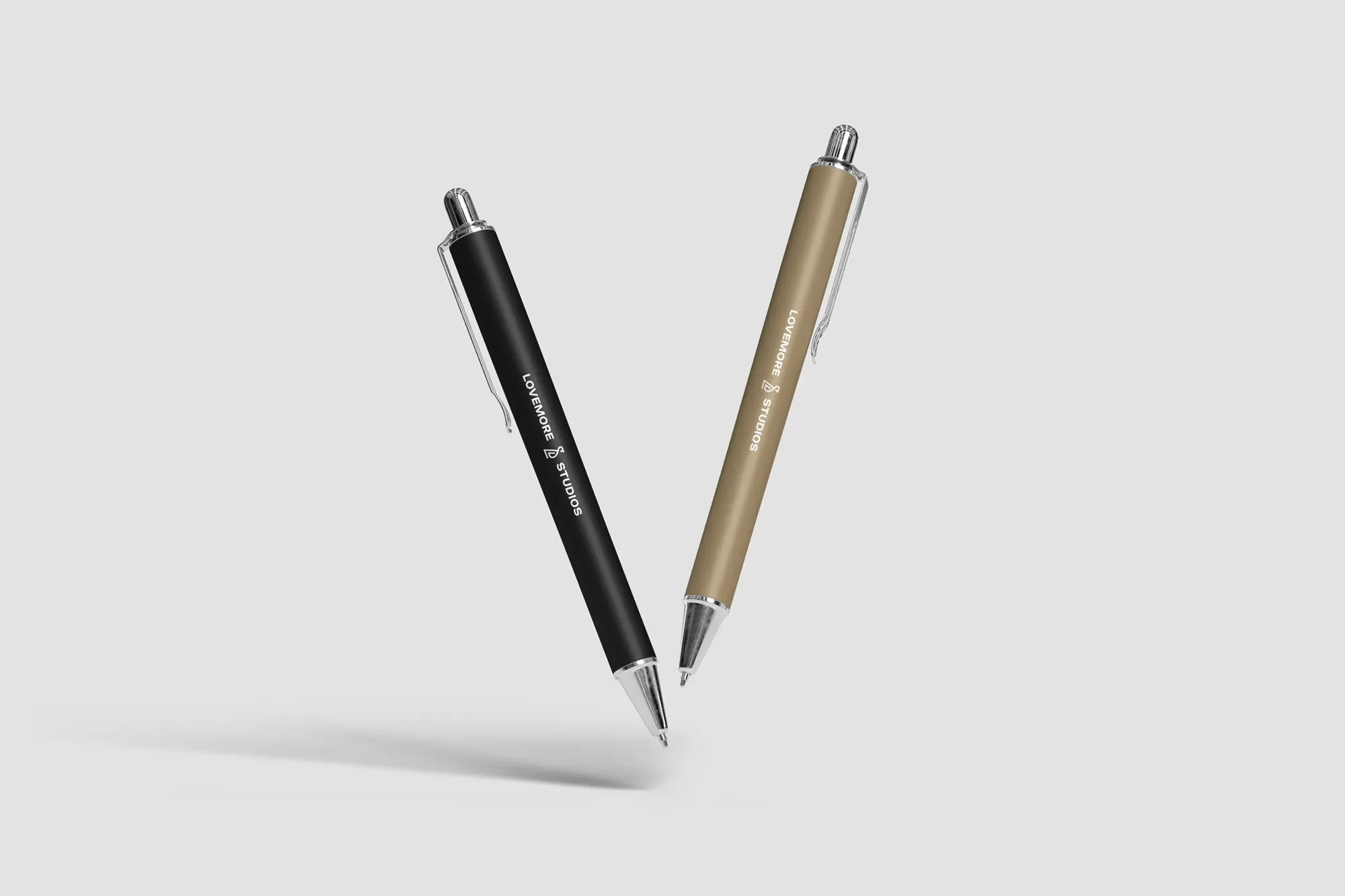 Two pens, one black and one beige, with metal tips, are positioned to form a heart shape against a plain light gray background.