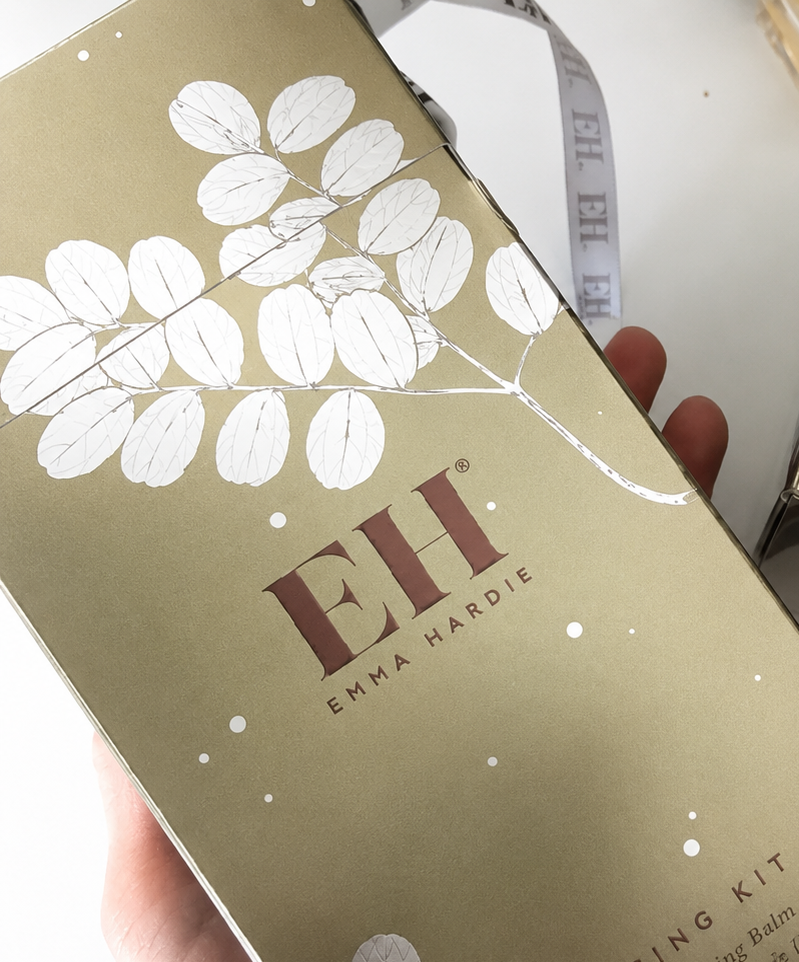 A gold-colored box with white leaf illustrations and the text "EH EMMA HARDIE" on the front, along with the words "GLOW GIFT SET" and "GIFTING KIT."
