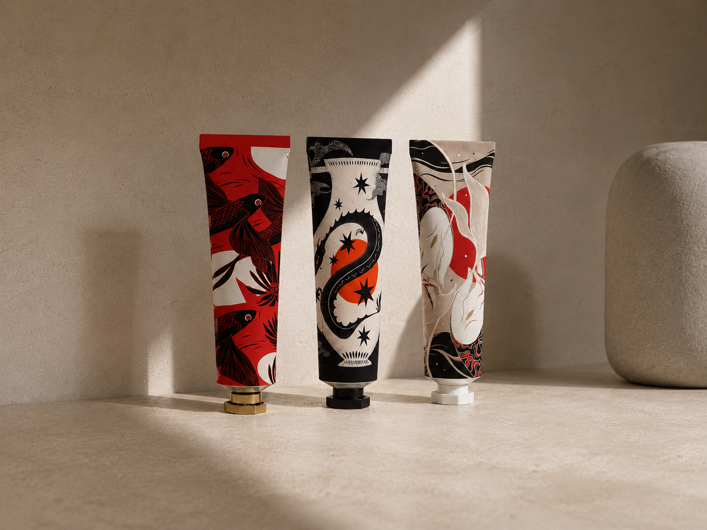 Three decorative tubes with colorful abstract patterns on a beige surface, with a large textured beige vase in the background on the right.
