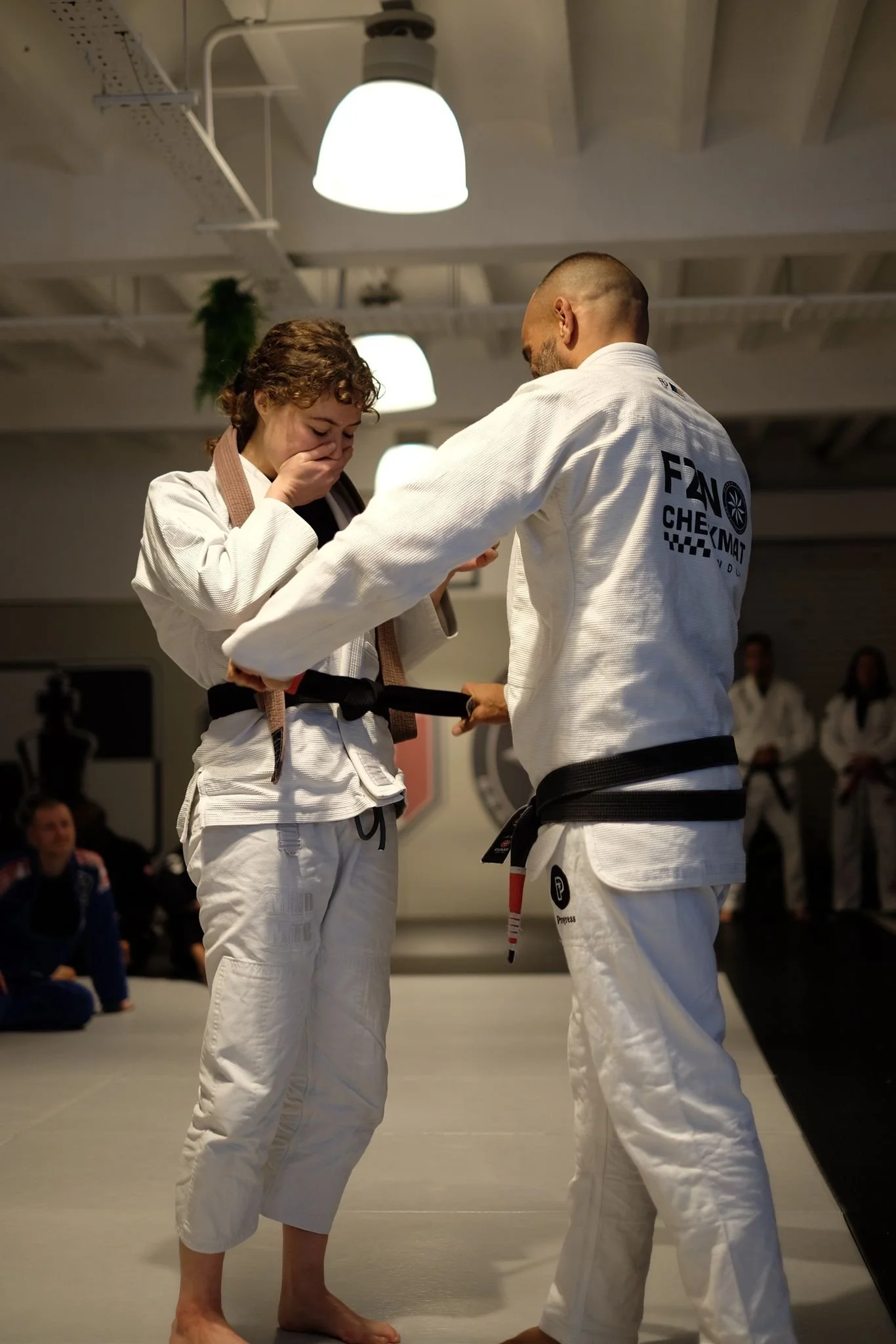 Two martial artists, one female and one male, dressed in white gis, are engaging in a training session in a dojo.