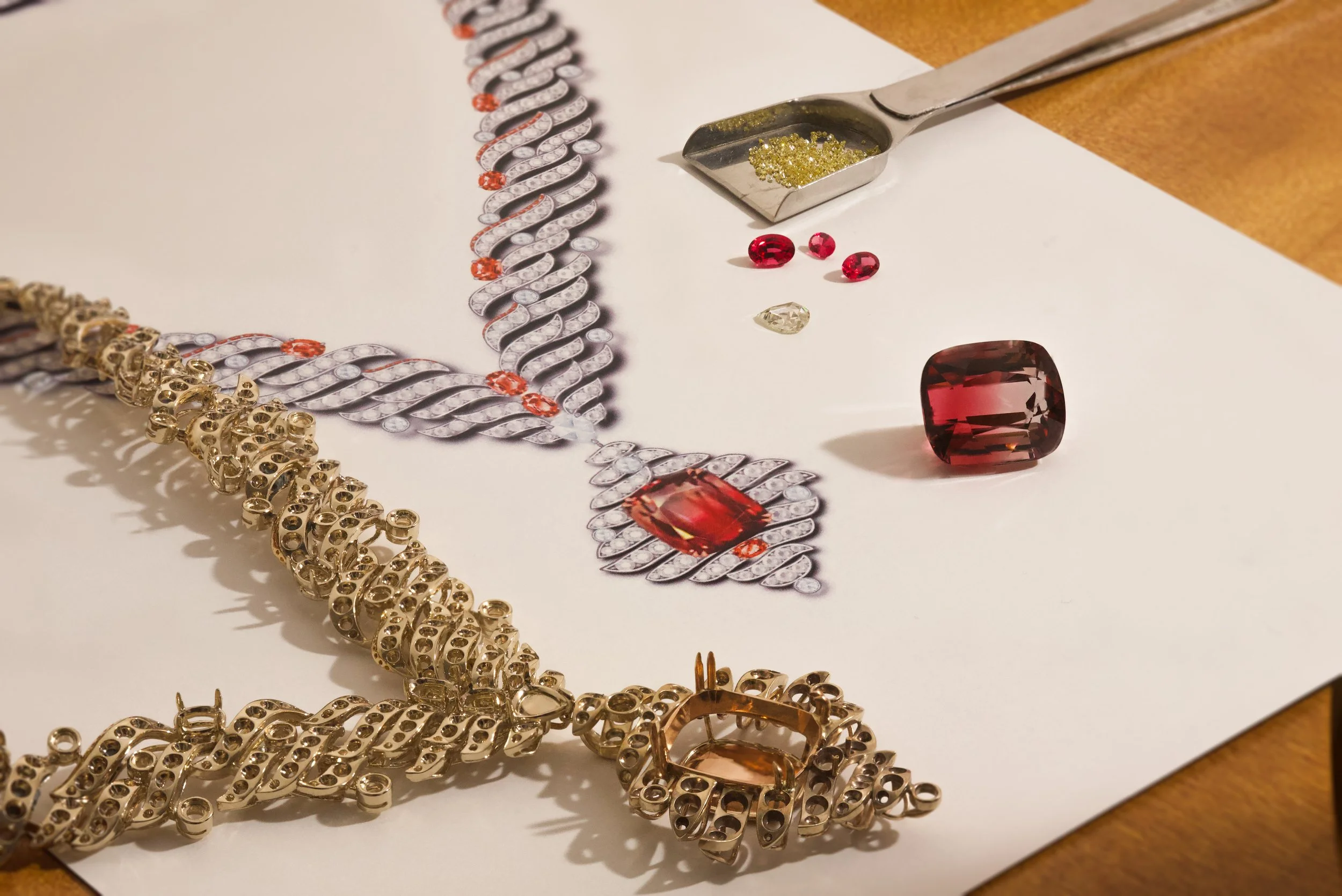 Jewelry making with gold and silver chains, rhinestones, gemstones, and a tray of yellow glitter on a white paper