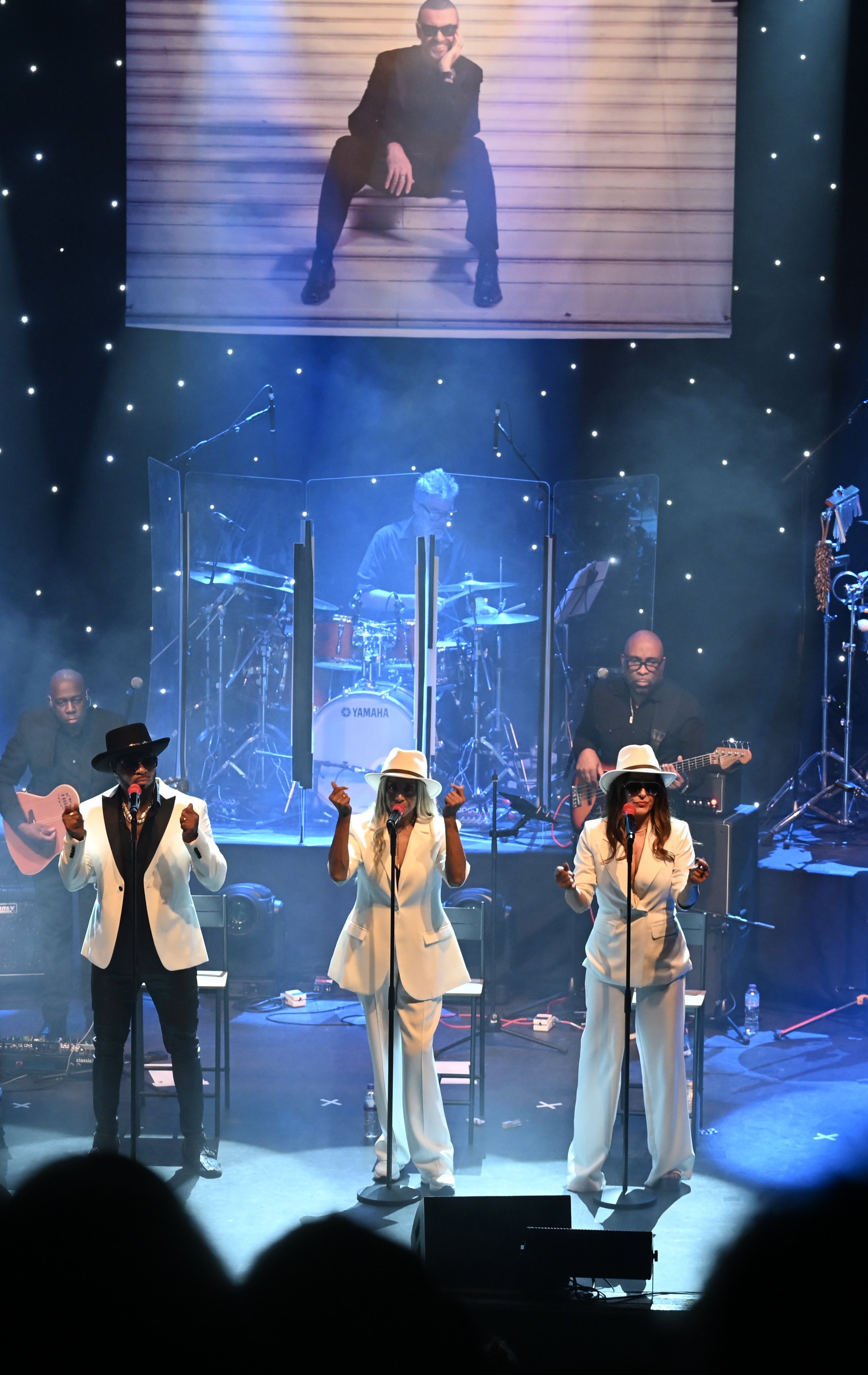 Live band performing on stage at Boogie Nights event, featuring musicians and vocalists with colorful lighting and balloons in the background.