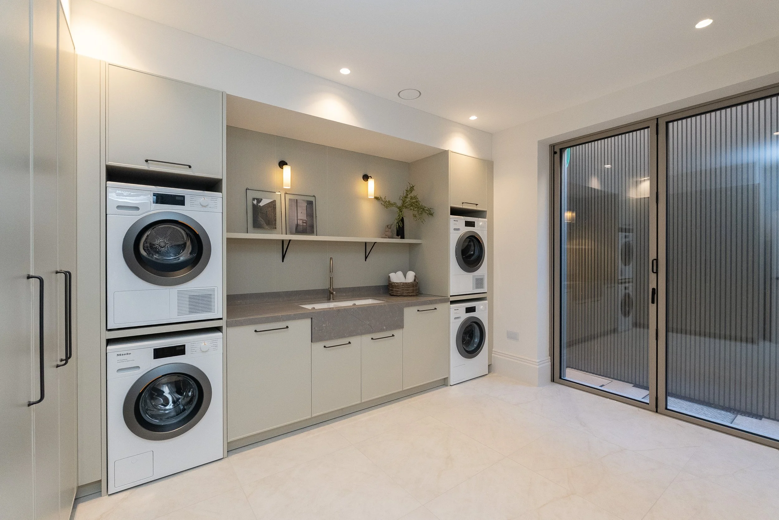 Modern laundry room with stacked washer and dryer, sink, and glass sliding door.