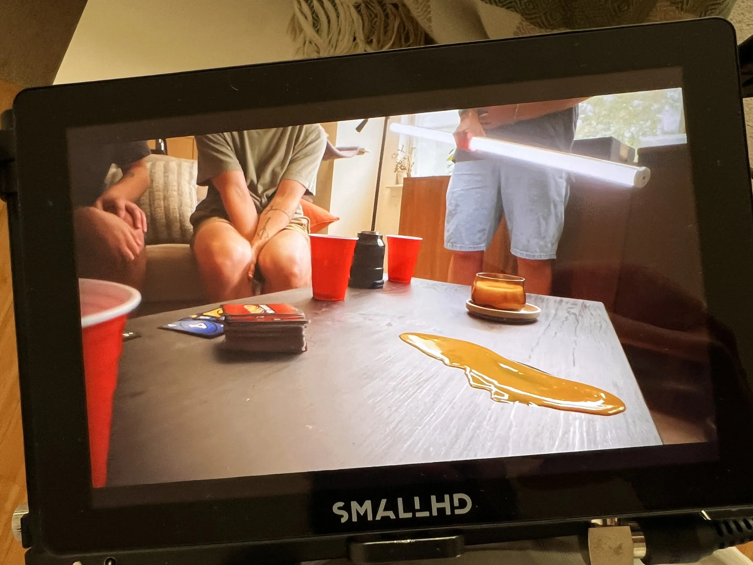 People sitting around a table with red cups, a stack of cards, and spilled liquid on the surface, inside a room with natural light.