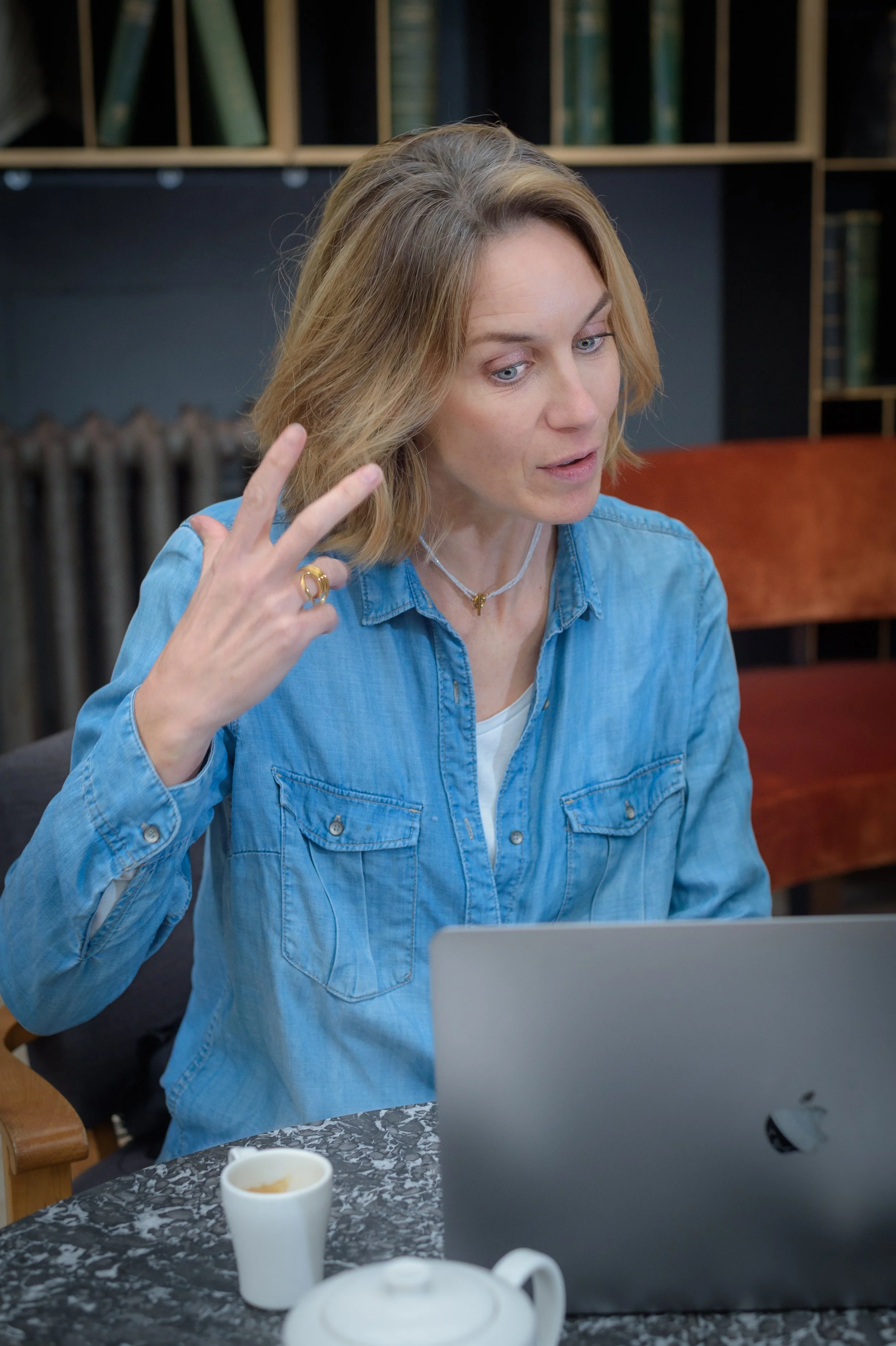 Femme assise à une table, regardant un ordinateur portable avec une expression concentrée, portant une chemise en denim.