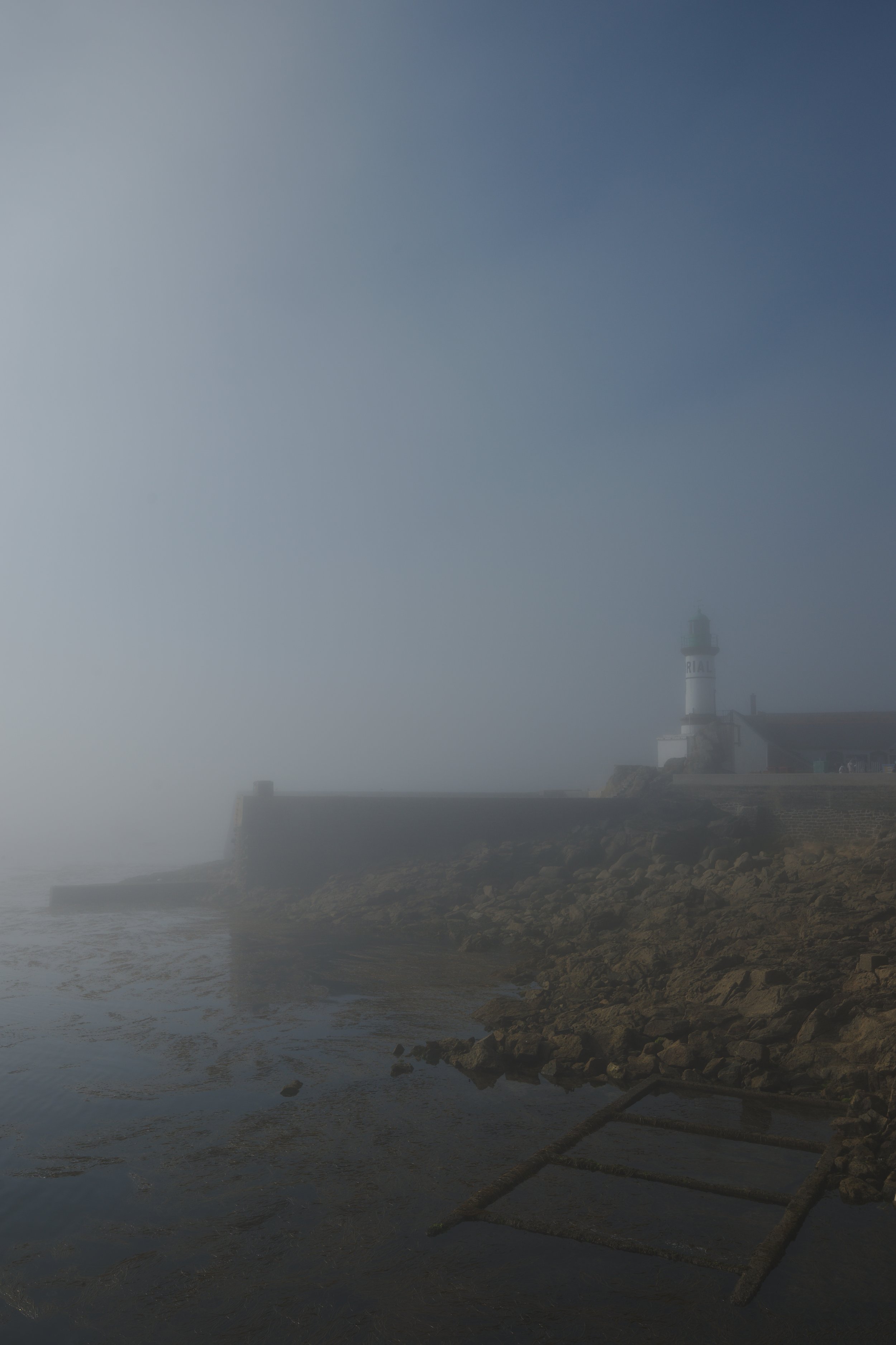 Phare sur une côte rocheuse enveloppée de brume, avec un filet de pêche en retrait dans l'eau.