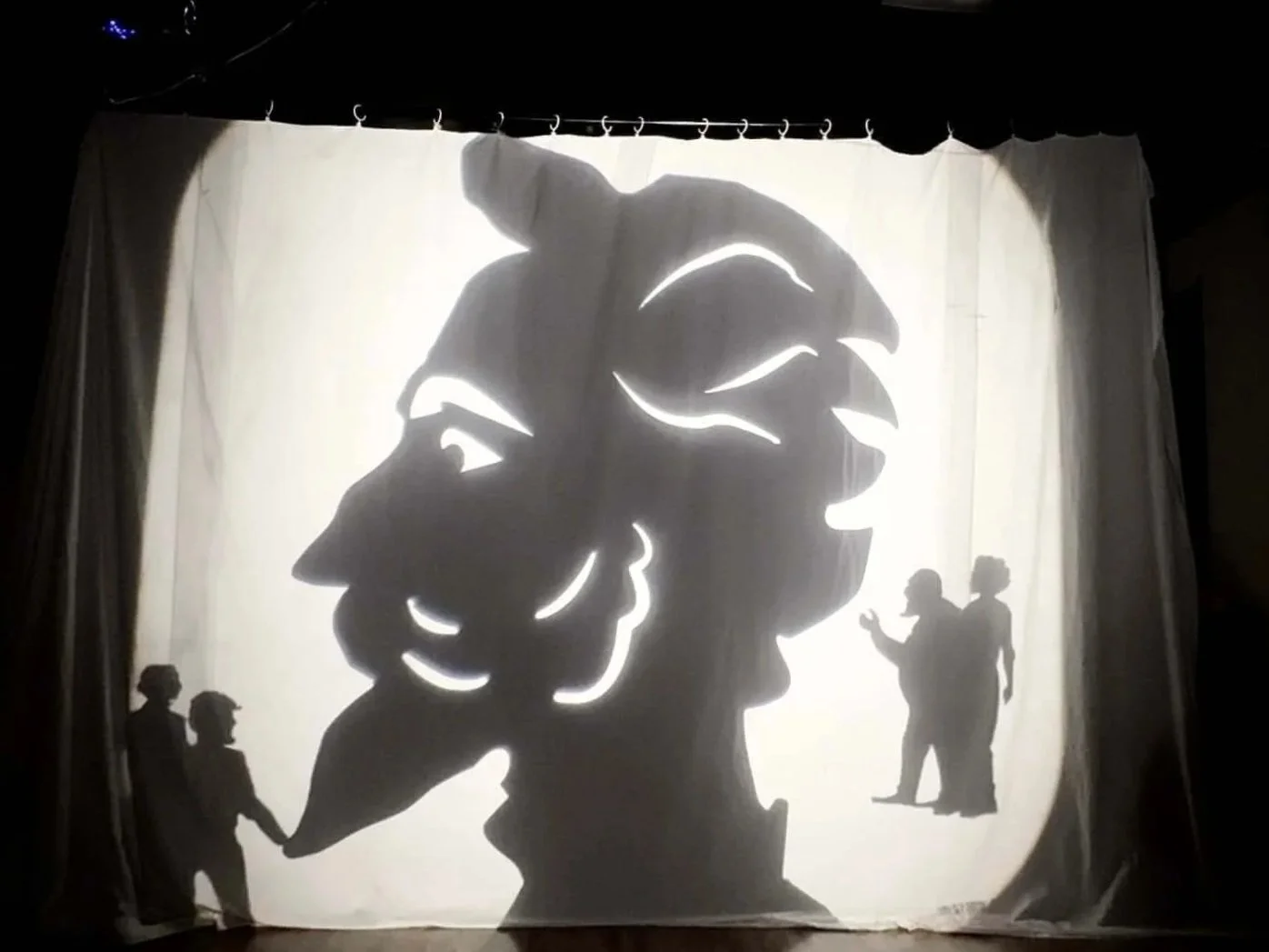 Silhouette of a large head on a backlit fabric, with smaller full body shadows surrounding it