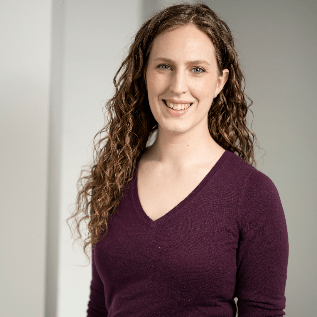 Headshot of a woman with long curly hair smiling at the camera and wearing a maroon v-neck top