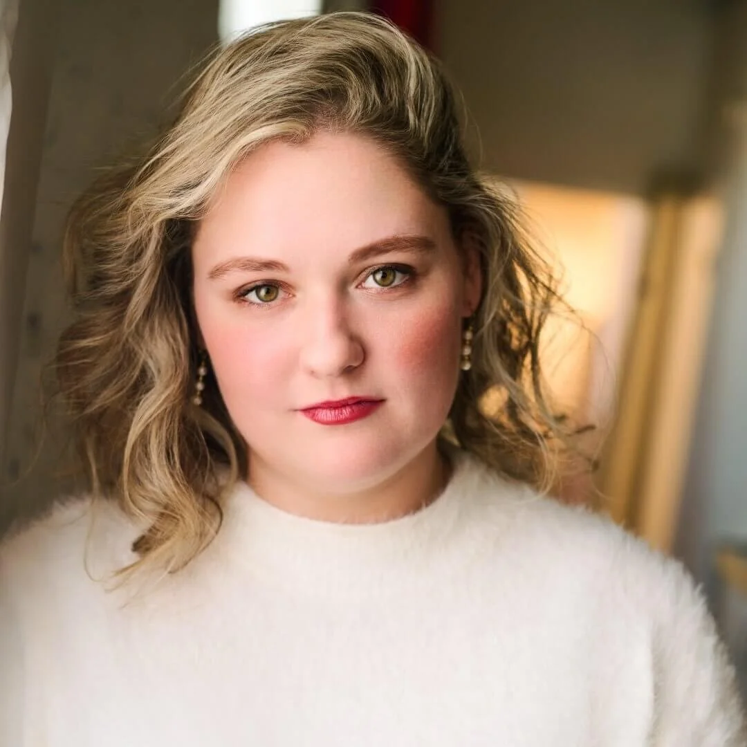 Headshot of woman with shoulder length blonde wavy hair wearing a white sweater