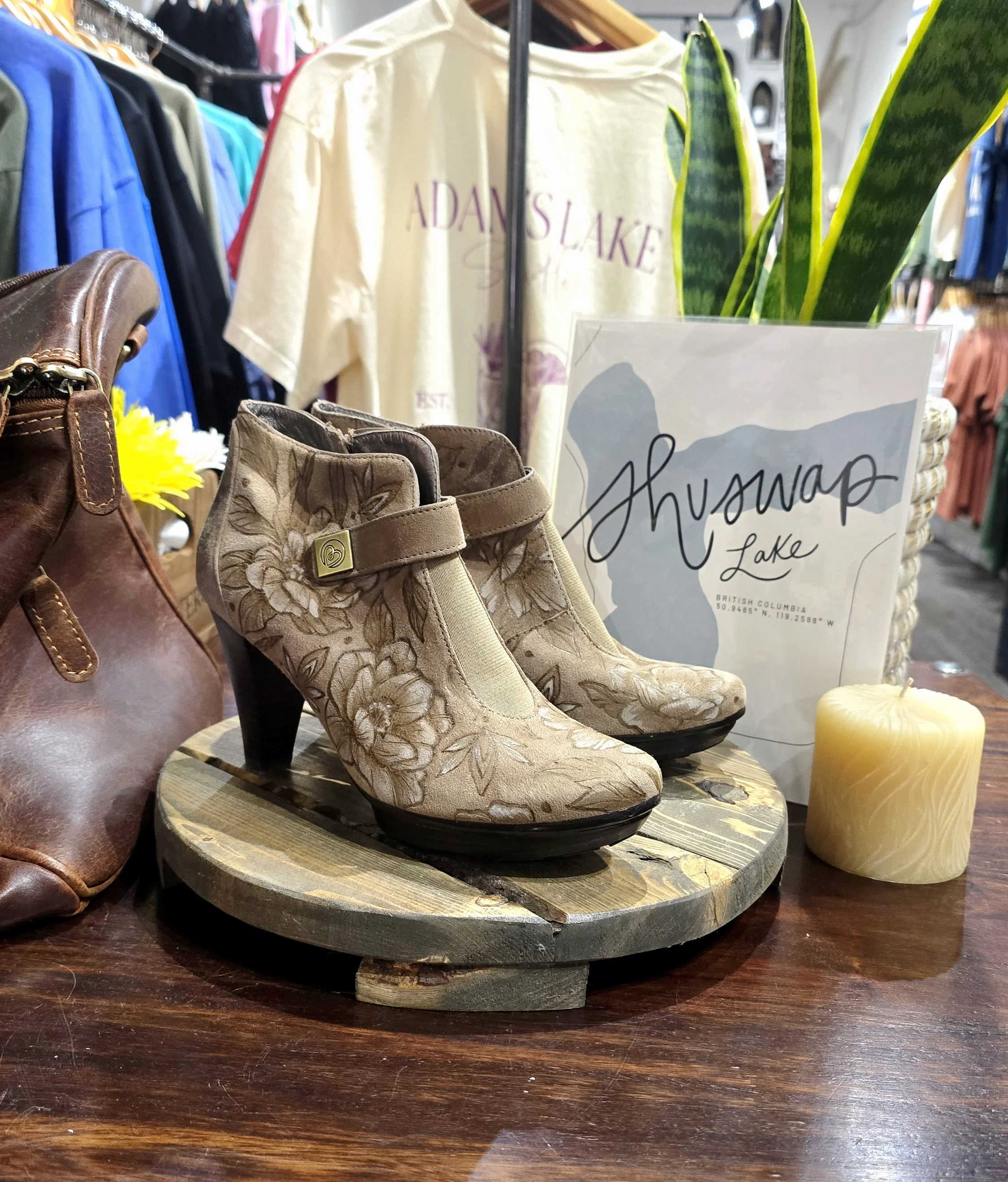 suede ankle boots designed by artist Dana Carlson sitting on a shelf in a local Salmon Arm store called on Alex with t shirts and Shuswap Lake sign