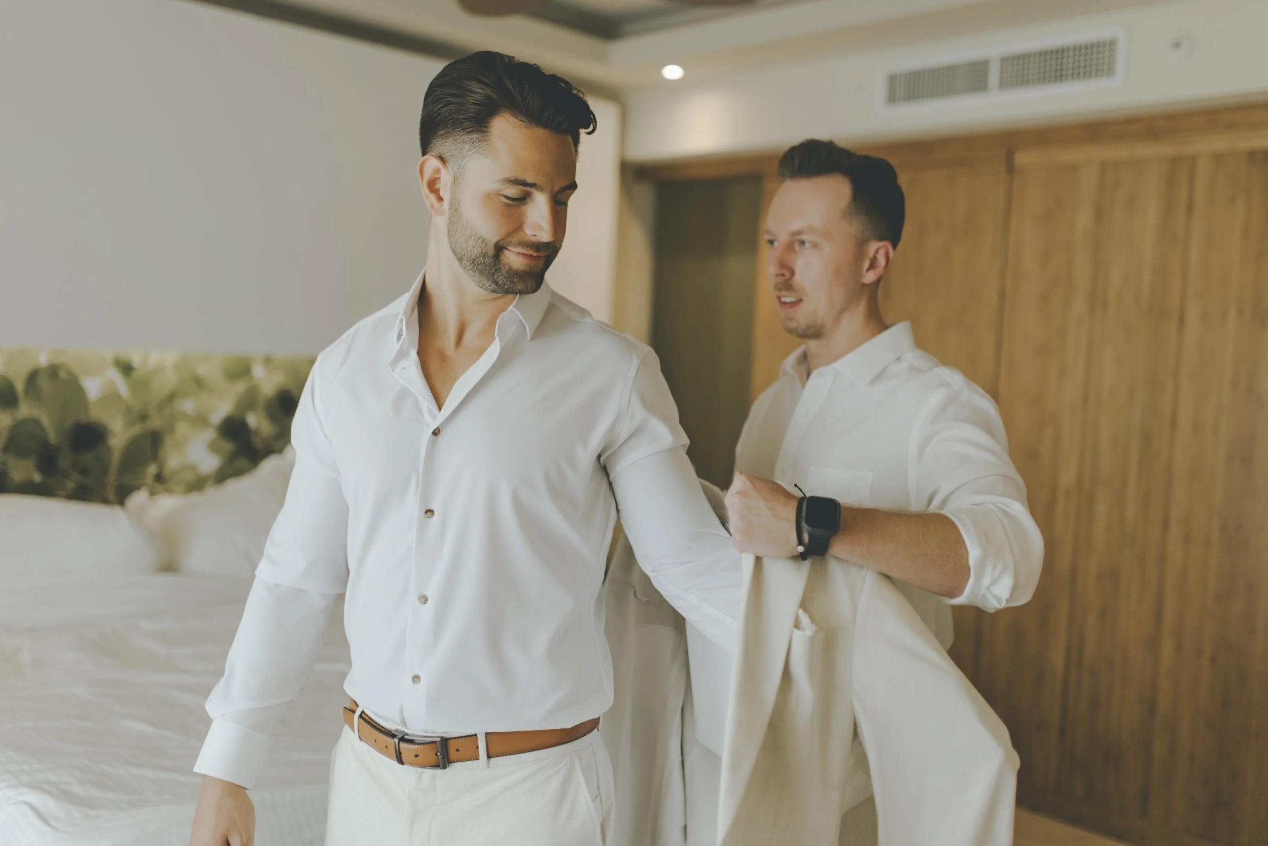 Groom getting ready with a groomsman helping him dress before a Punta Cana destination wedding