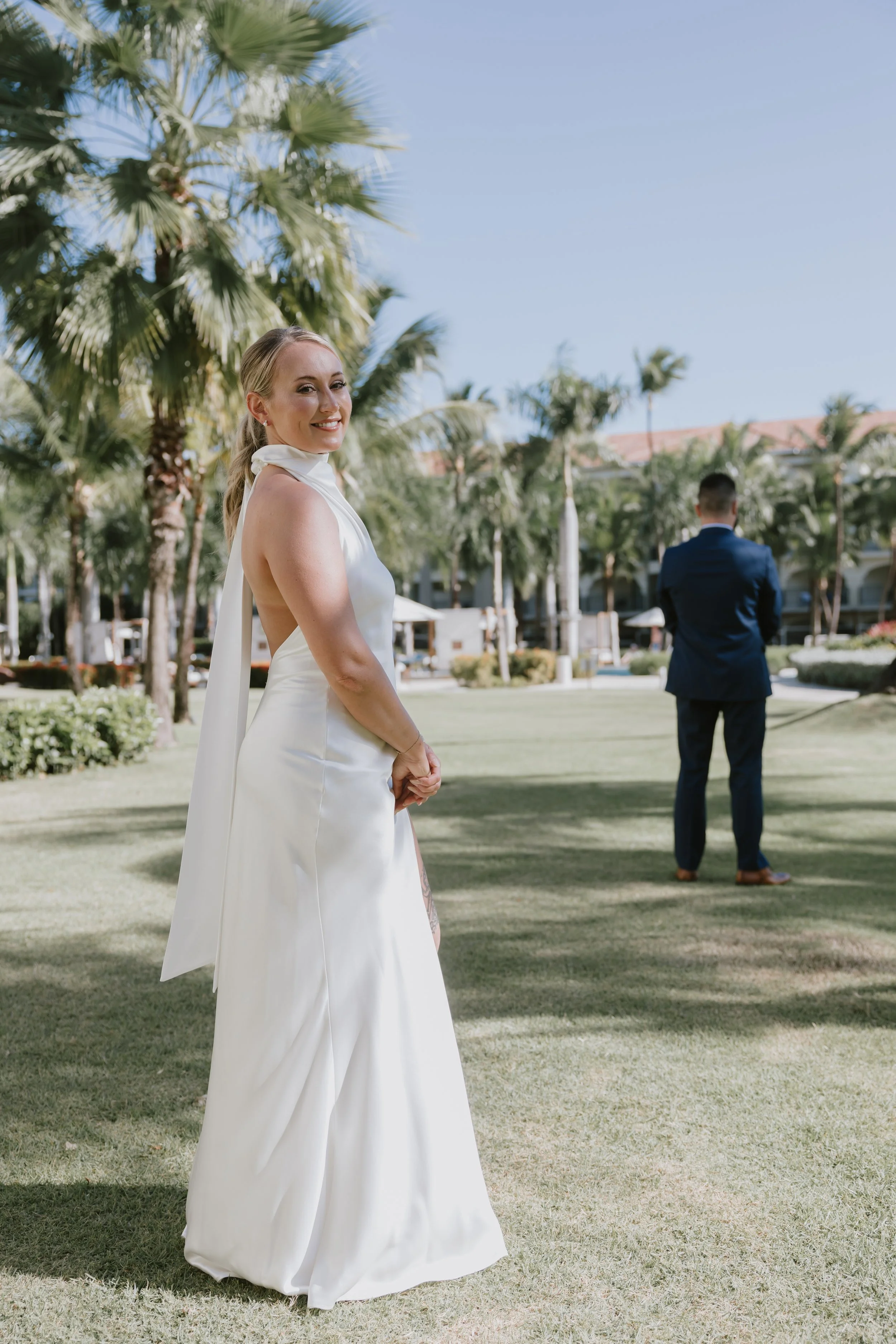 Bride glancing back over her shoulder with her groom walking behind her at Dreams Royal Beach