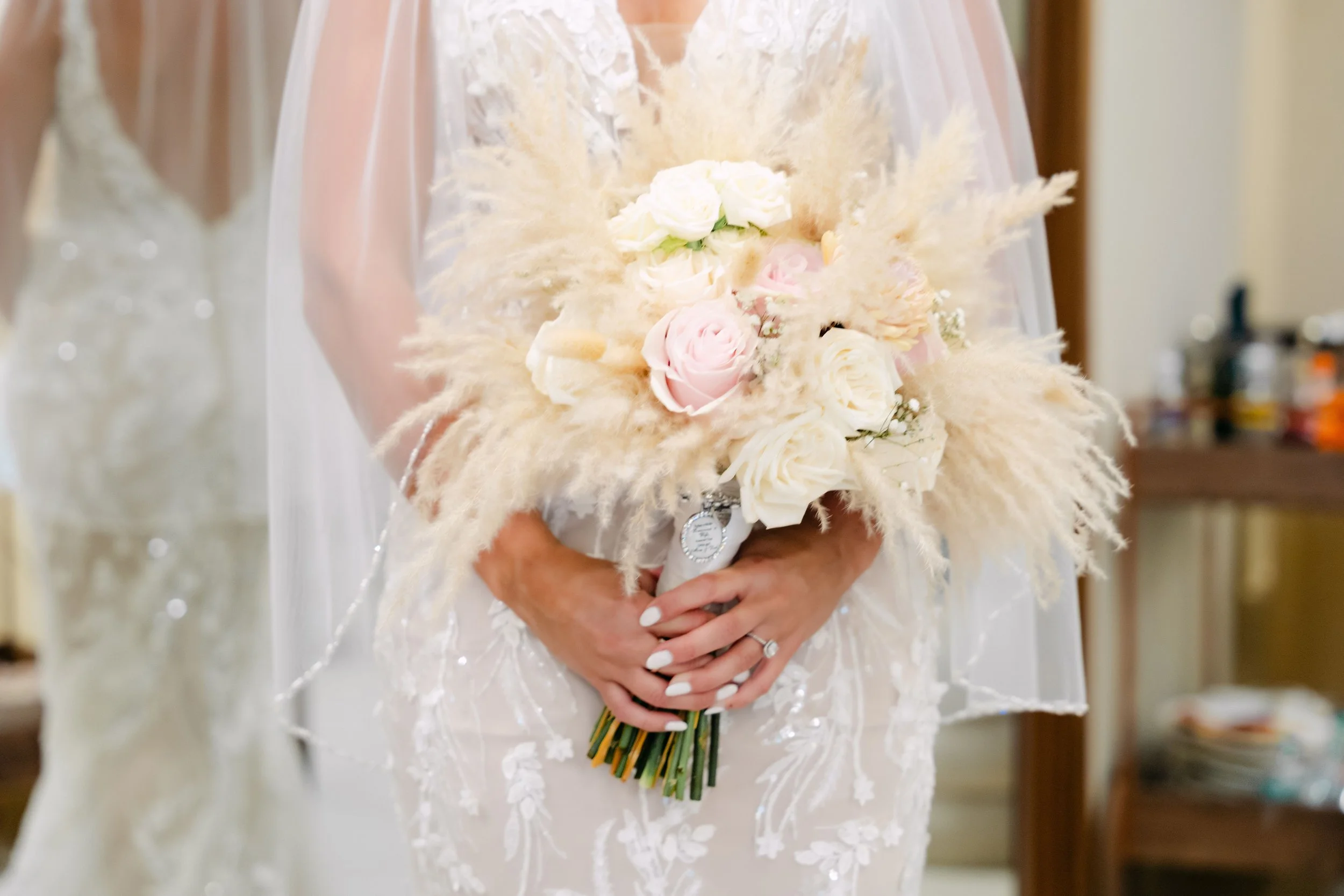 Bride holding an elegant bridal bouquet with white roses, blush roses, and pampas grass while wearing a lace wedding dress during her destination wedding in Punta Cana, Dominican Republic.