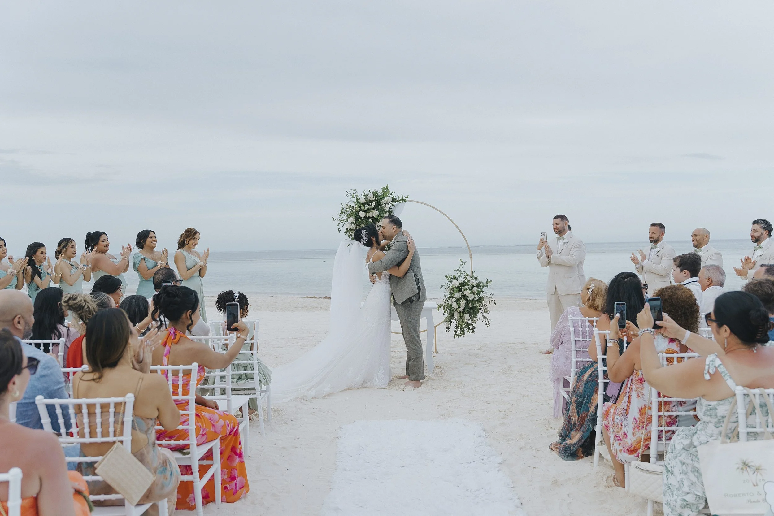 Guests watching bride and groom kiss on the beach aisle