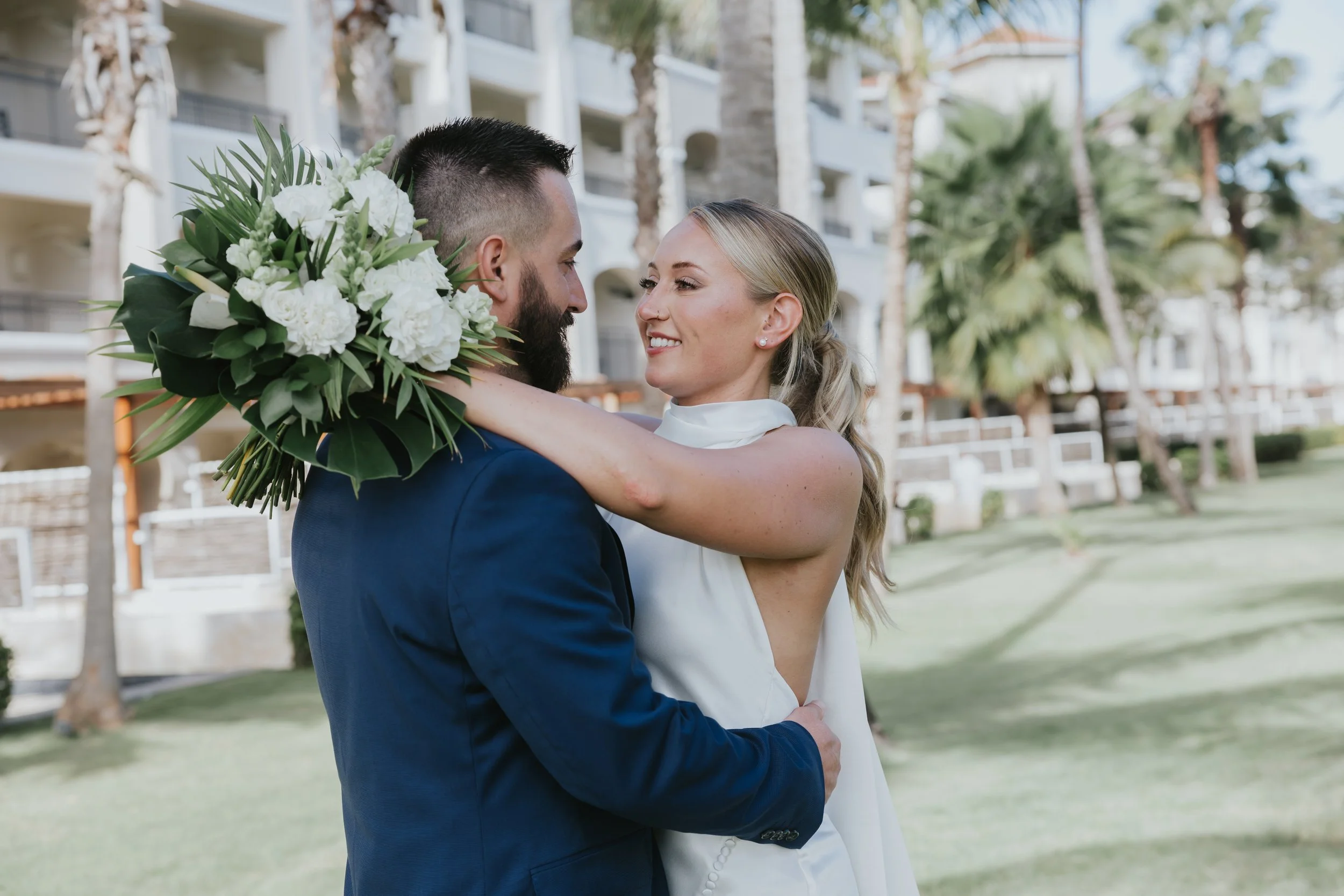 Groom holding bride's bouquet while embracing her on the lawn at Dreams Royal Beach