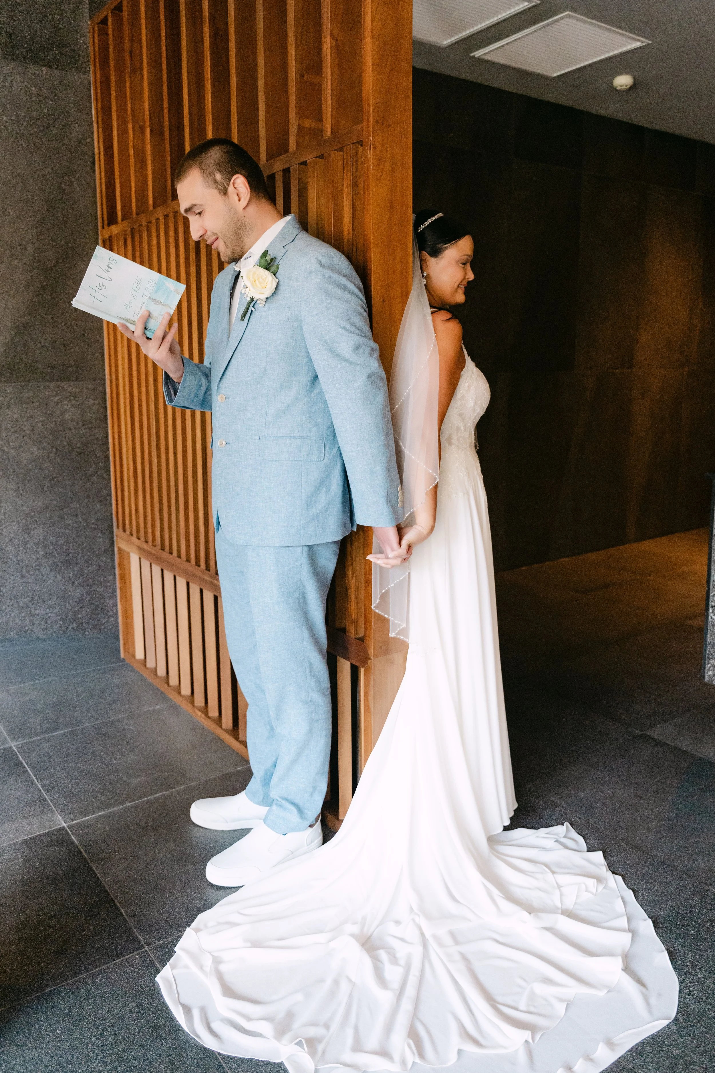 Groom reading a handwritten note from his bride during their first look in a modern wood-slat courtyard at Dreams Flora