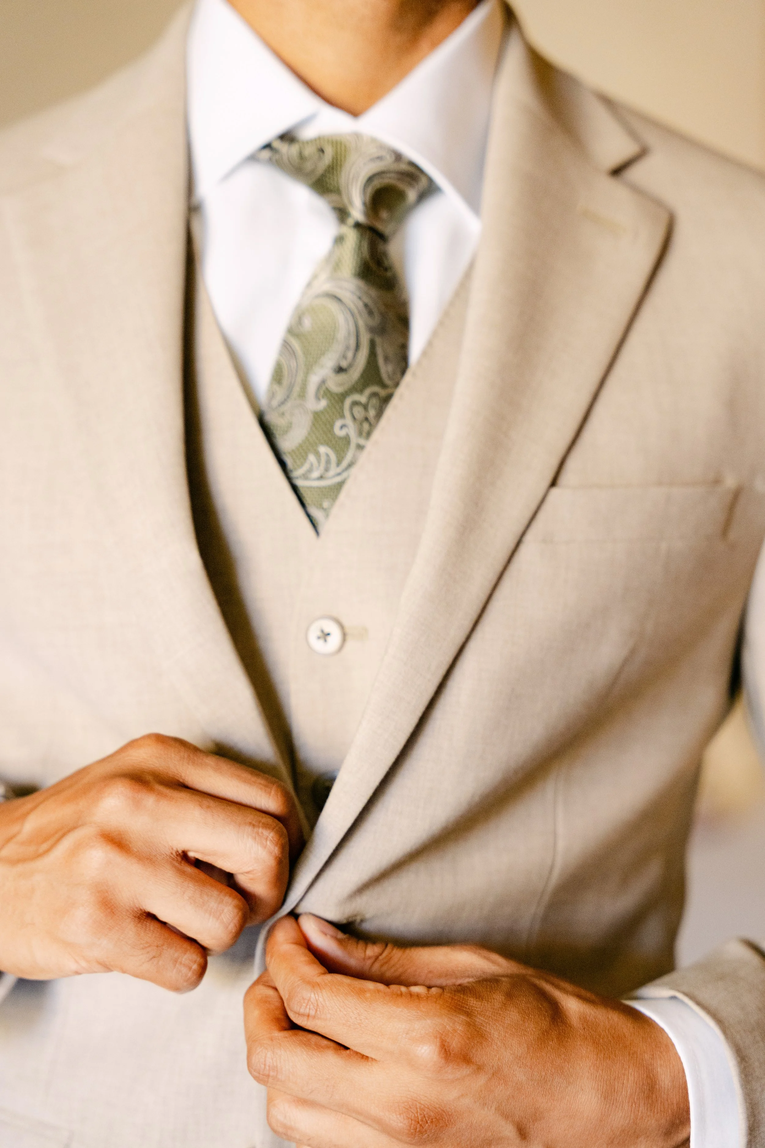 Groom in a tan three-piece suit and green patterned tie adjusting his jacket at Dreams Onyx Punta Cana