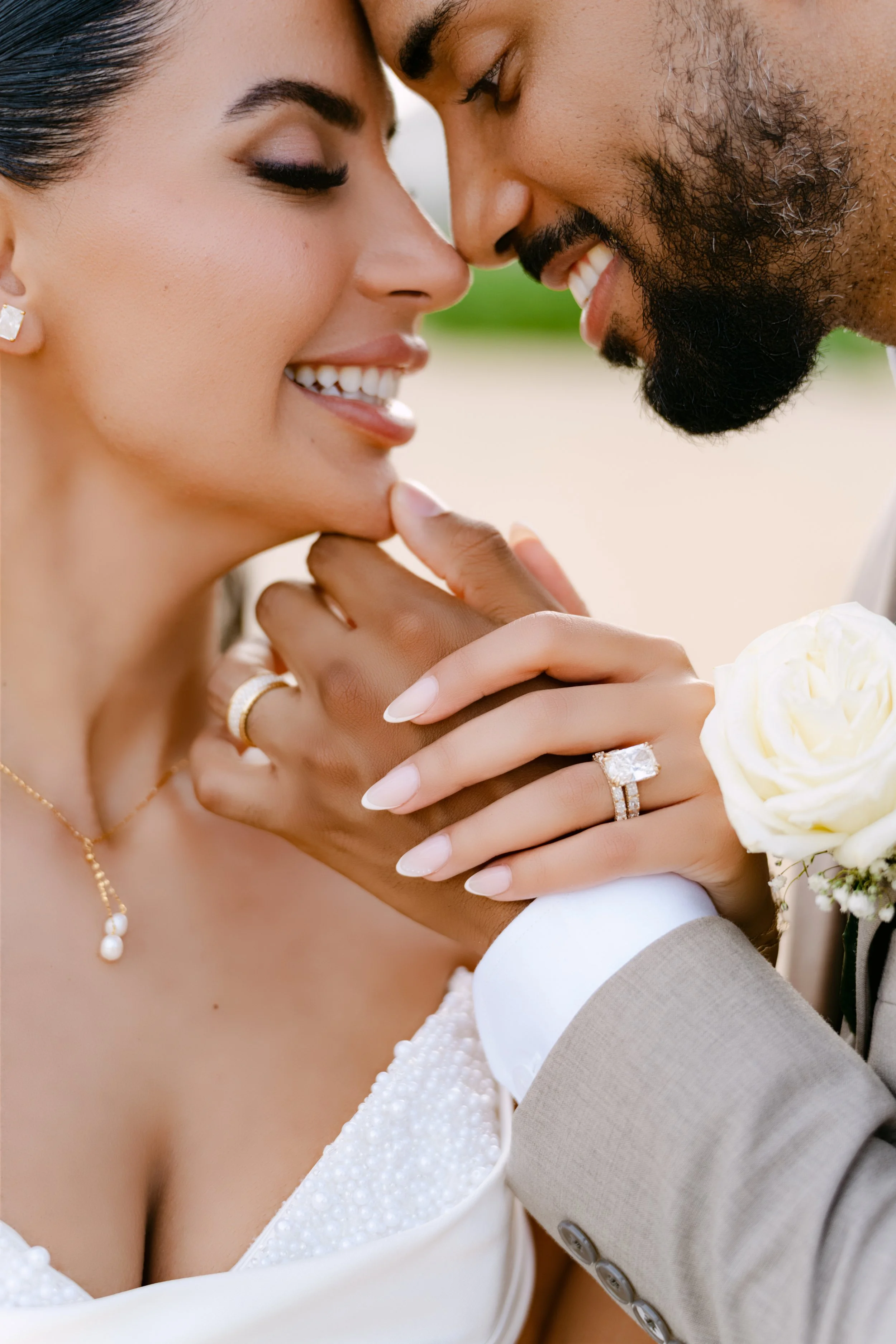 Close-up of the bride smiling with her ring hand held up beside a white rose