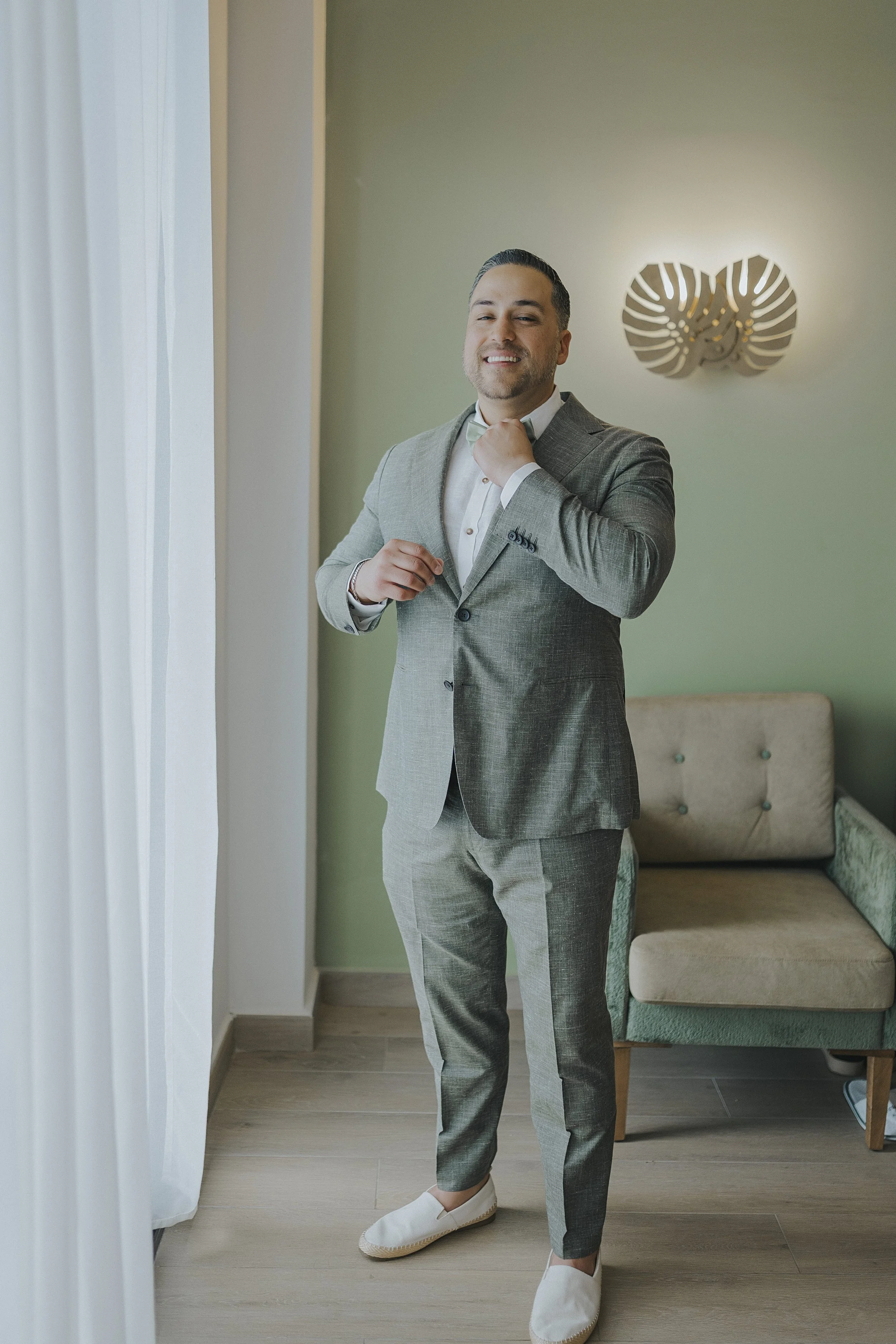 Groom getting ready in a sage green suit before the beach ceremony at Serenade Punta Cana