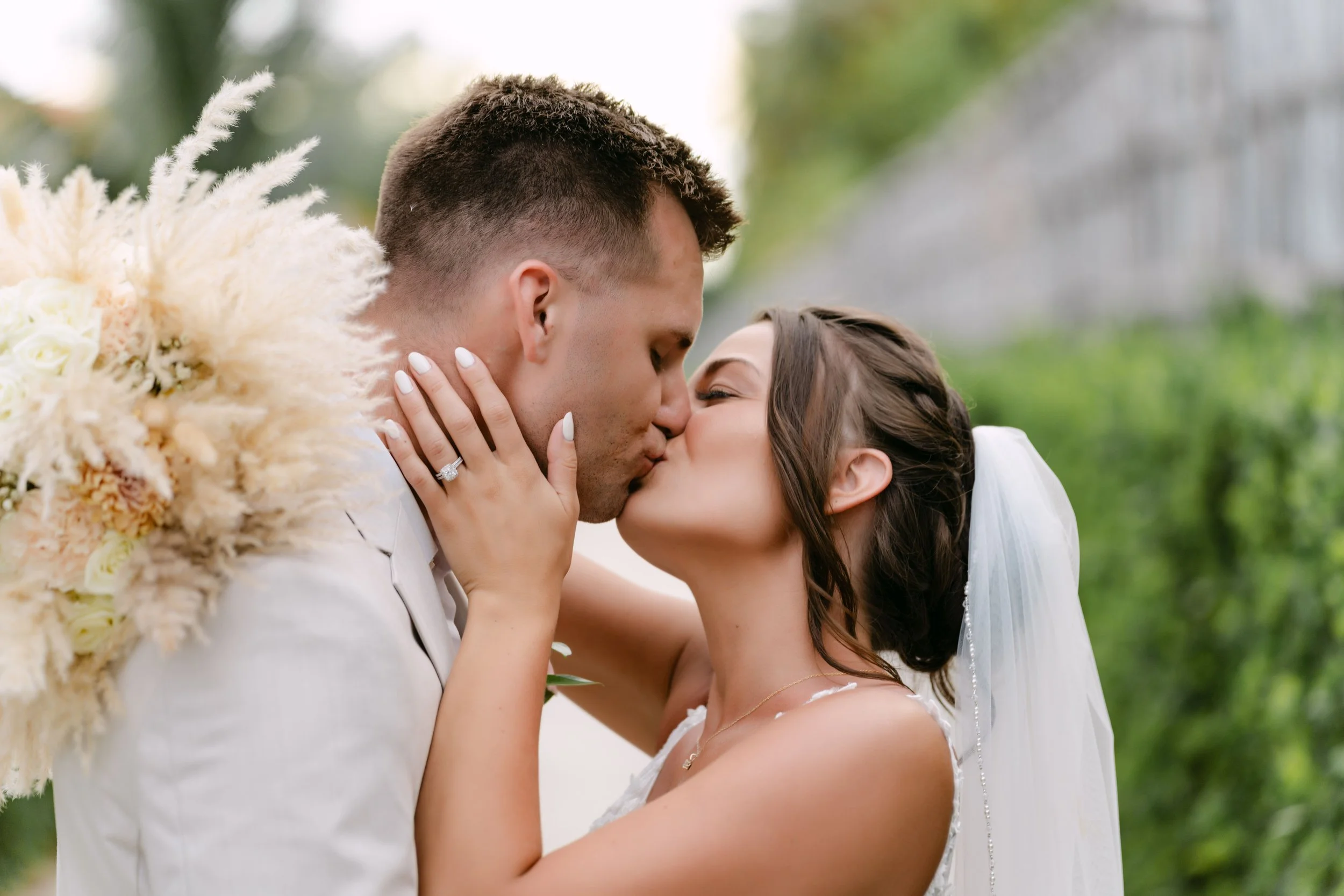 Bride and groom sharing a romantic kiss during their destination wedding portraits in Punta Cana, with the bride's bouquet, engagement ring, and elegant veil beautifully showcased.