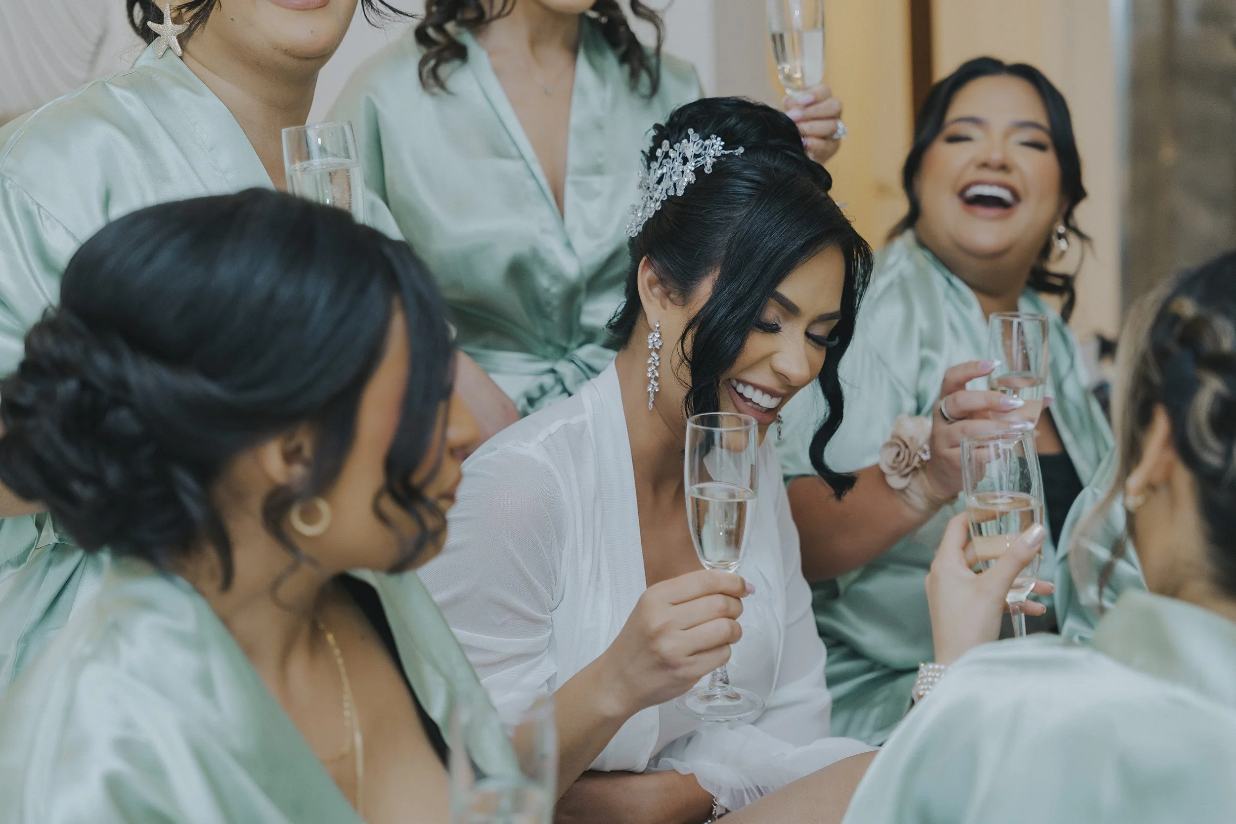 Bridesmaids celebrating in matching sage robes with a champagne toast