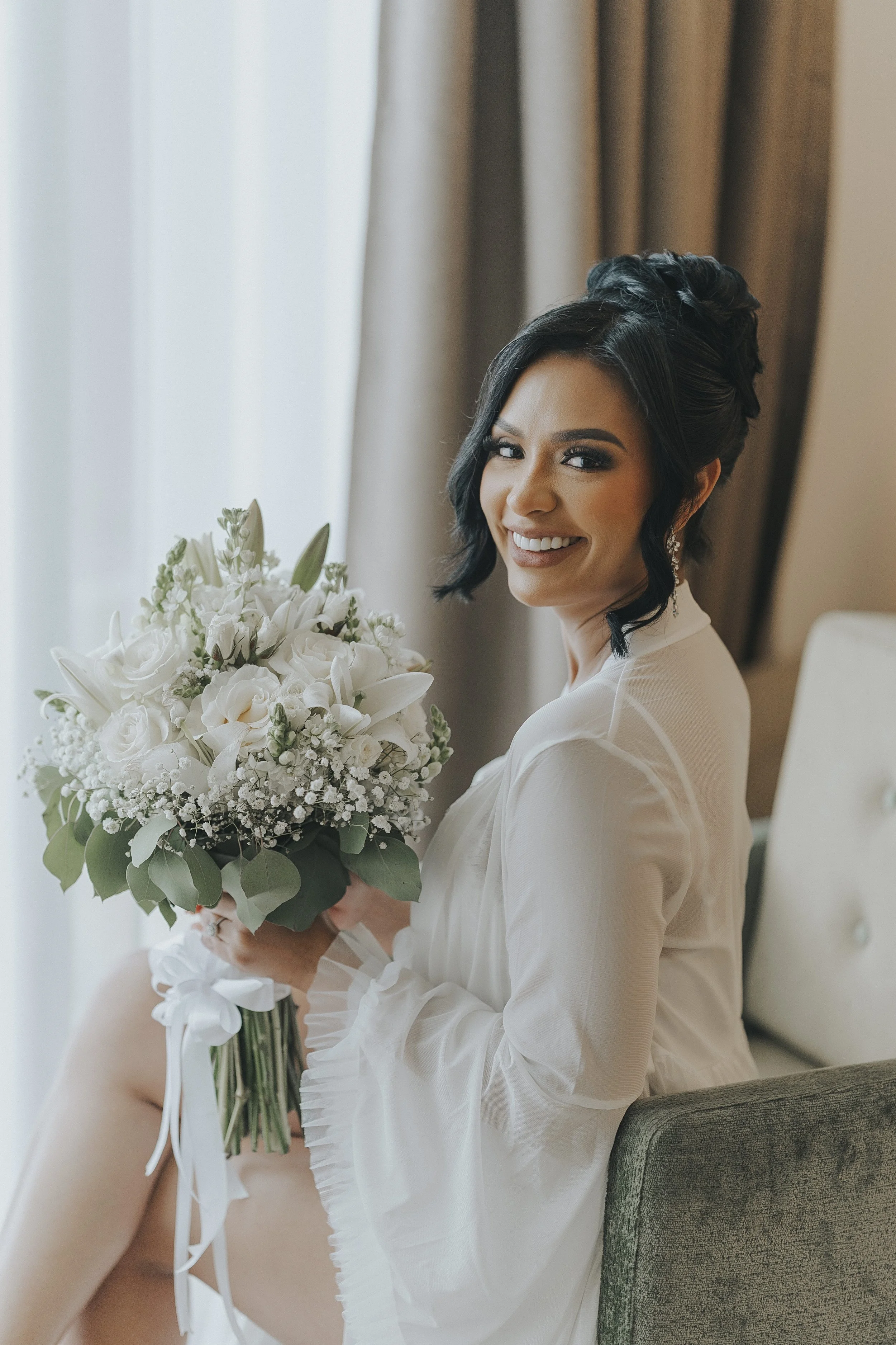Bride glowing in her robe with her white rose and baby's breath bouquet