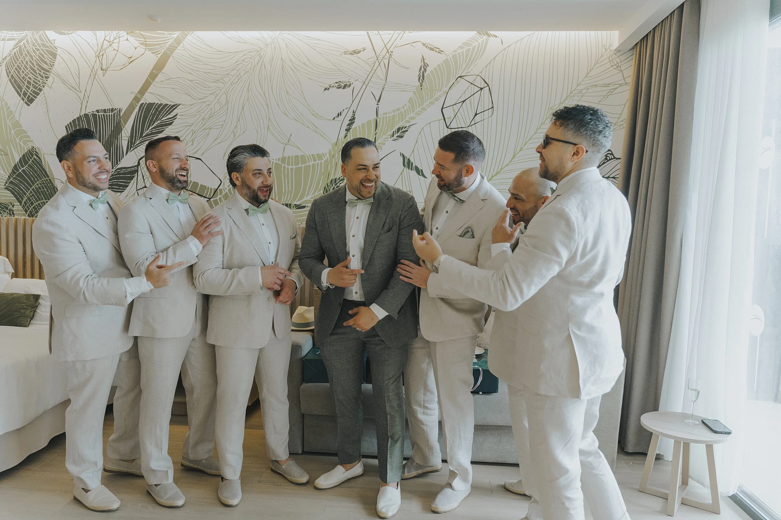 Groom and groomsmen sharing a laugh in matching cream linen suits before the ceremony