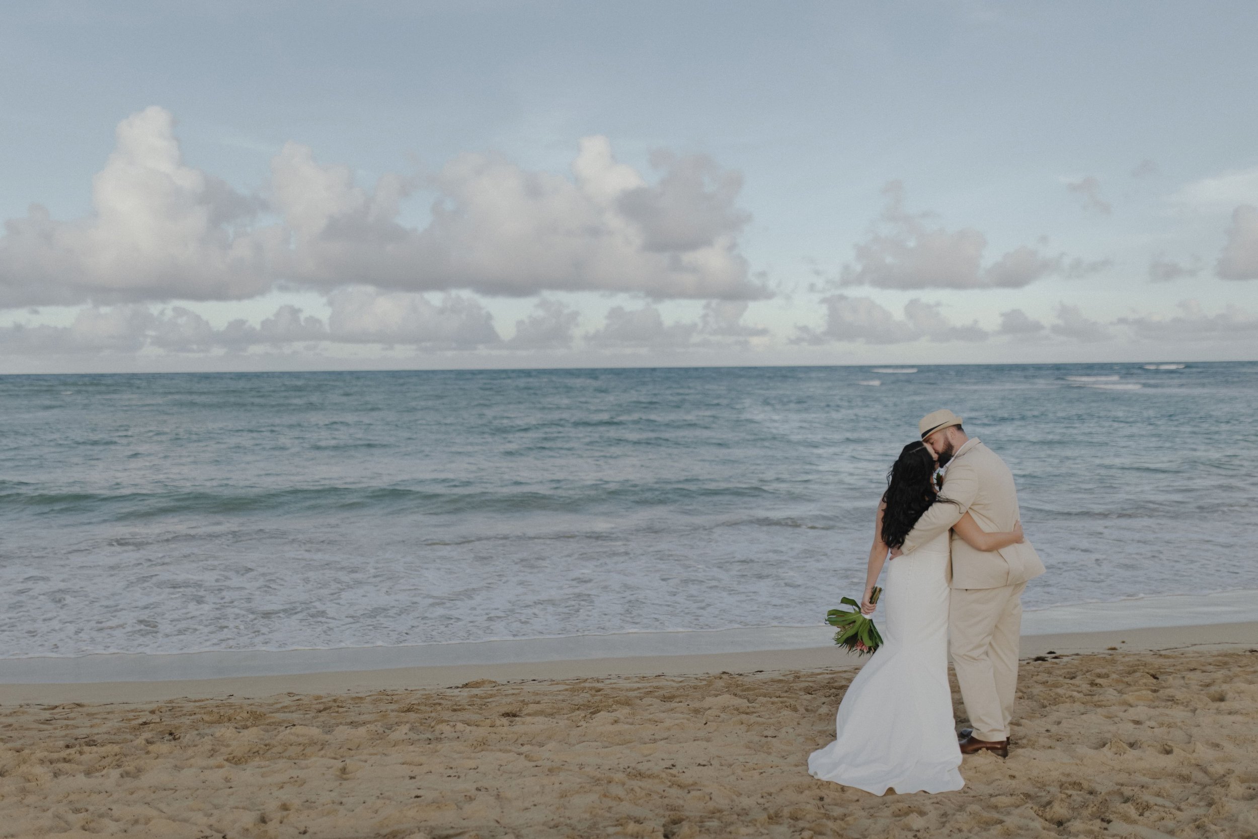 Bride and groom embracing at the water's edge with a wide ocean and sky view at Secrets Tides