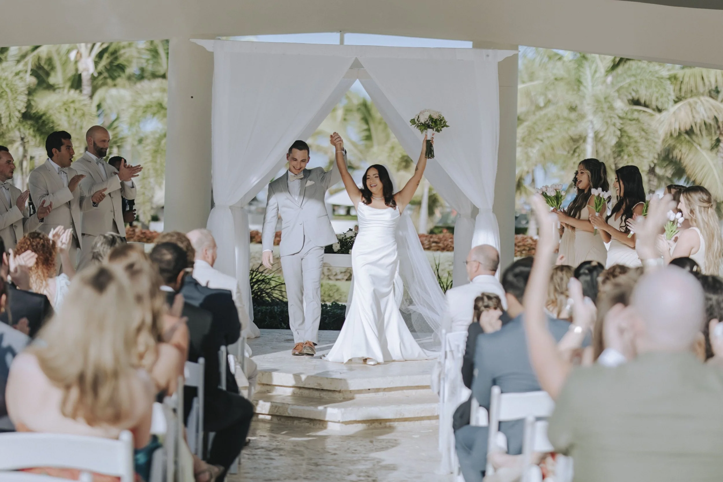 Bride and groom celebrating with raised hands as they walk back down the aisle after their Dreams Onyx wedding ceremony