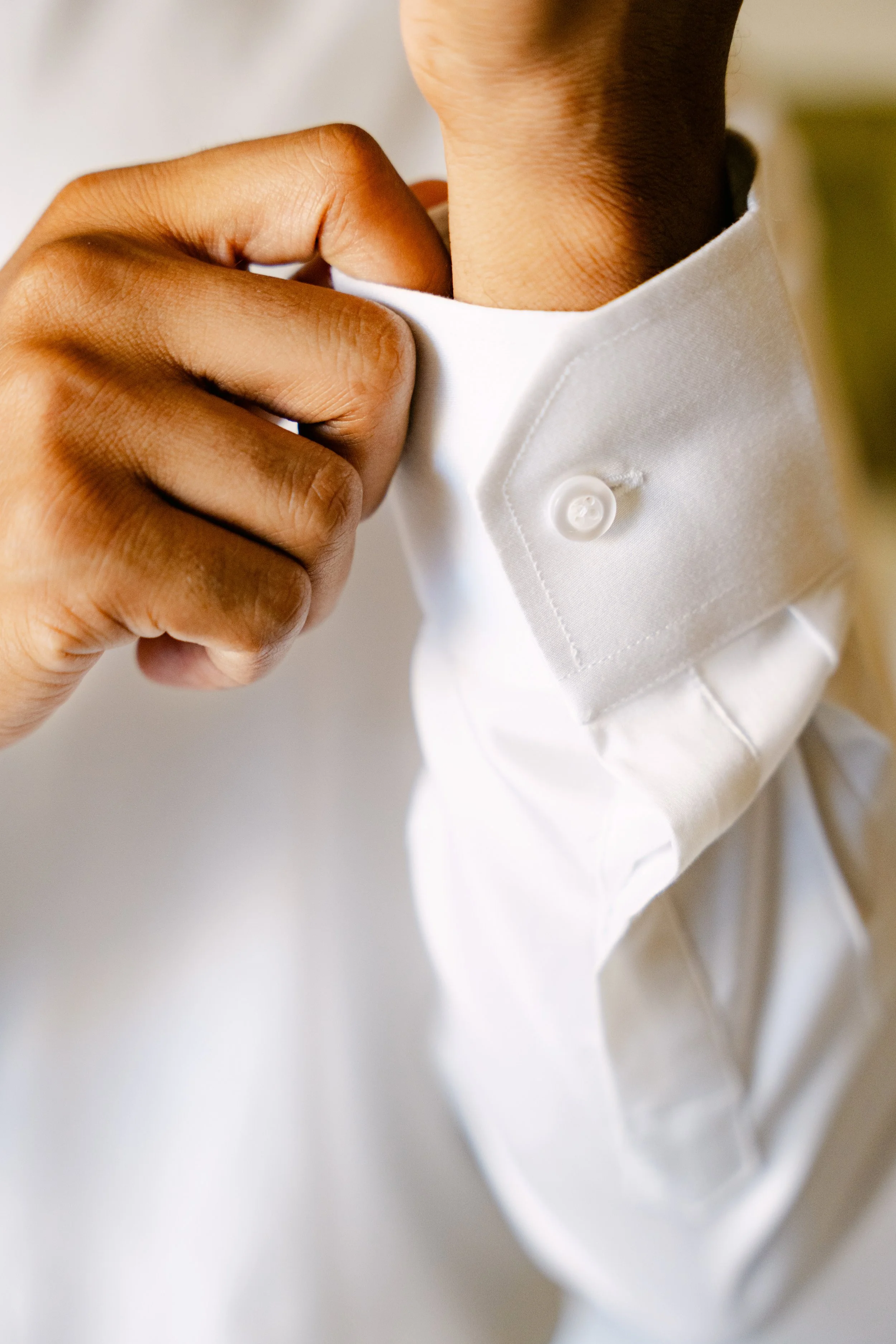 Groom’s hands fastening his white dress shirt while getting ready for the wedding