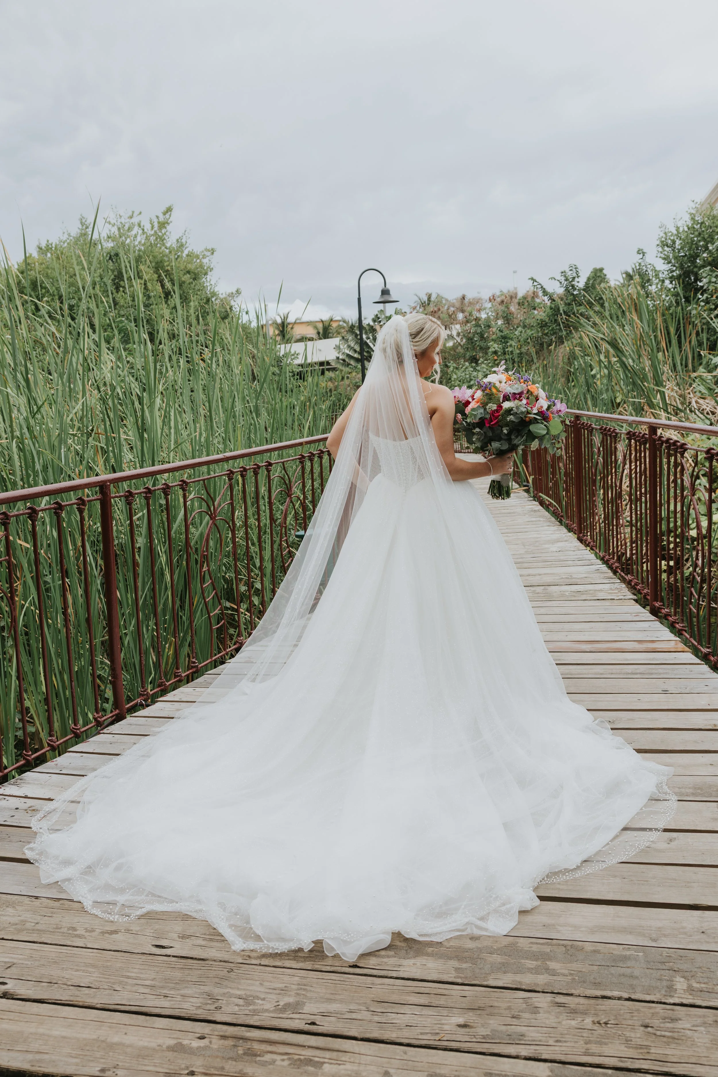 Bride in cathedral veil and ballgown crossing a wooden garden bridge with her bouquet at Majestic Elegance Punta Cana