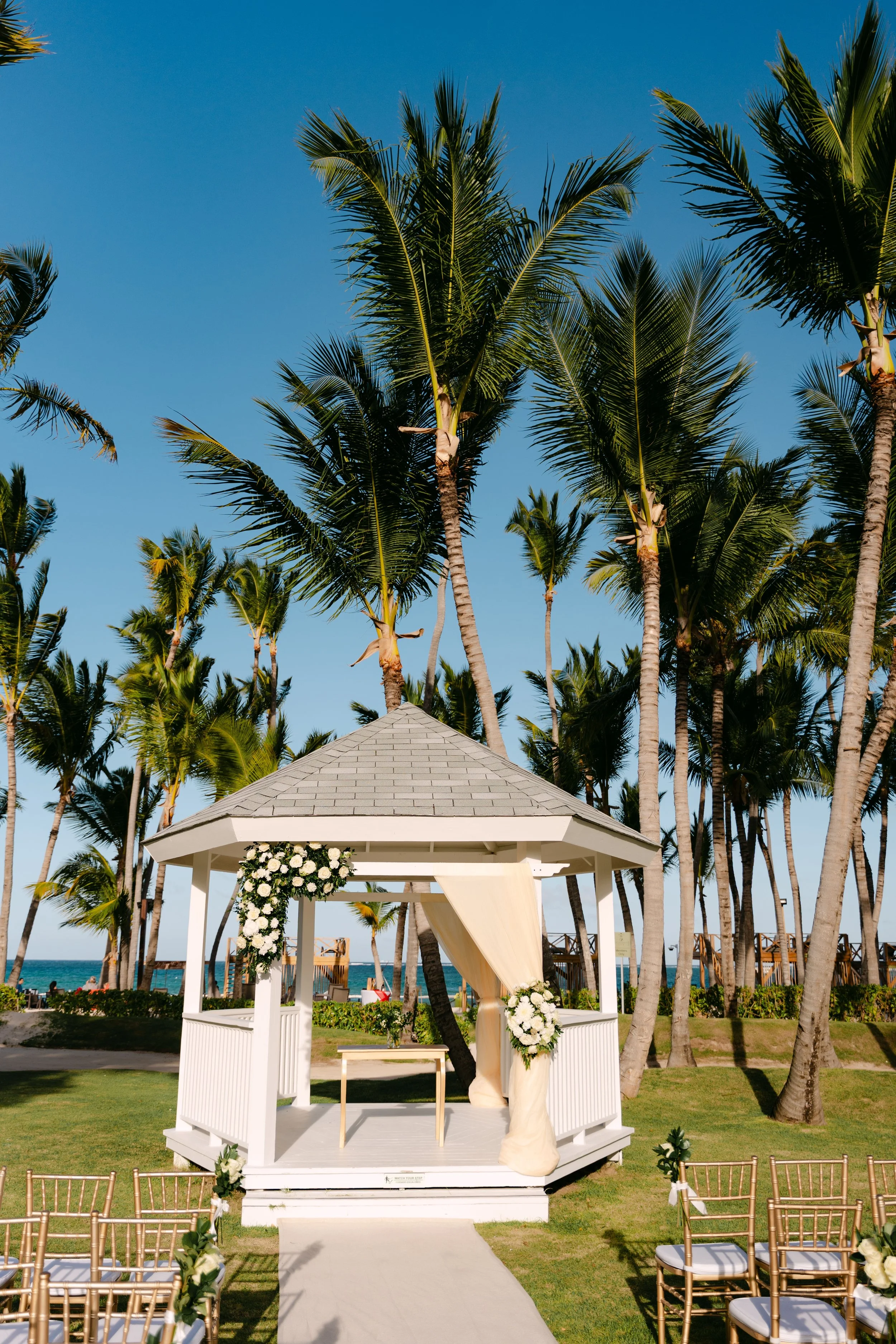 White gazebo decorated with florals for a garden ceremony, lined with palm trees at Dreams Flora
