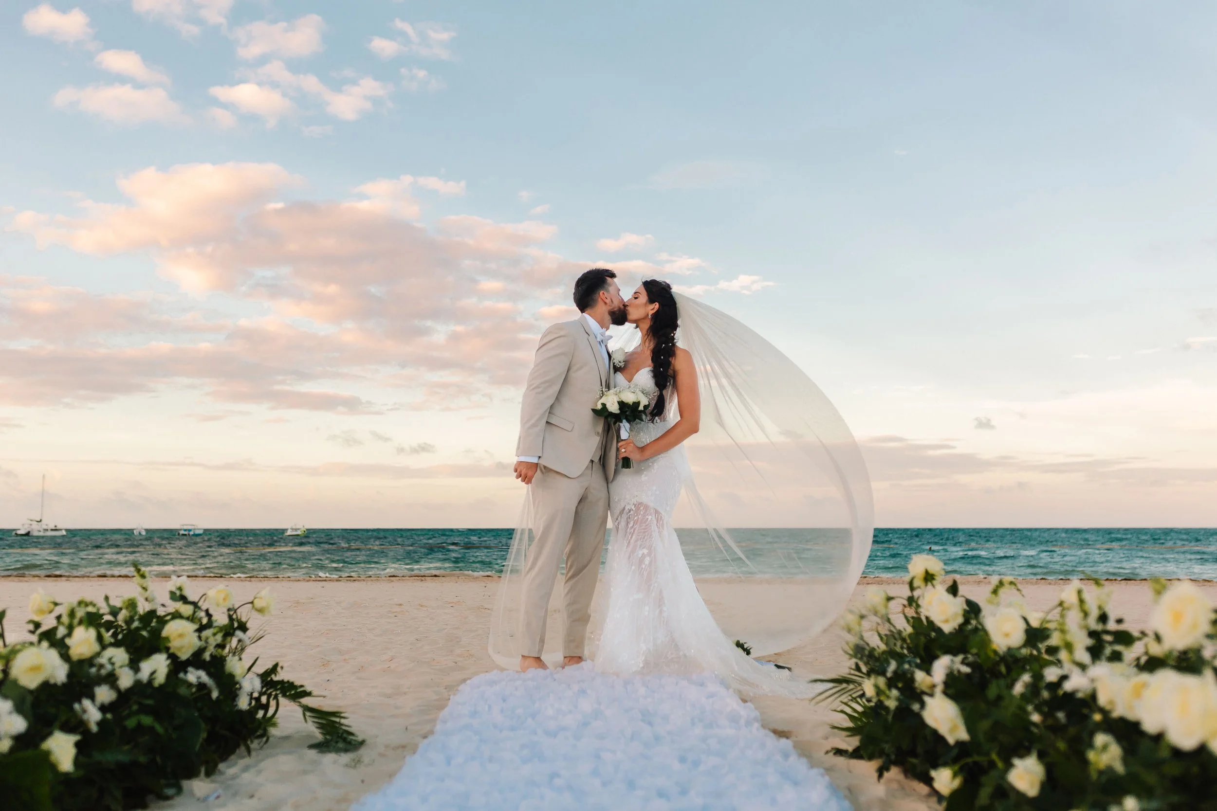 Bride and groom kissing on the beach with veil framing the ocean at Secrets Royal Beach