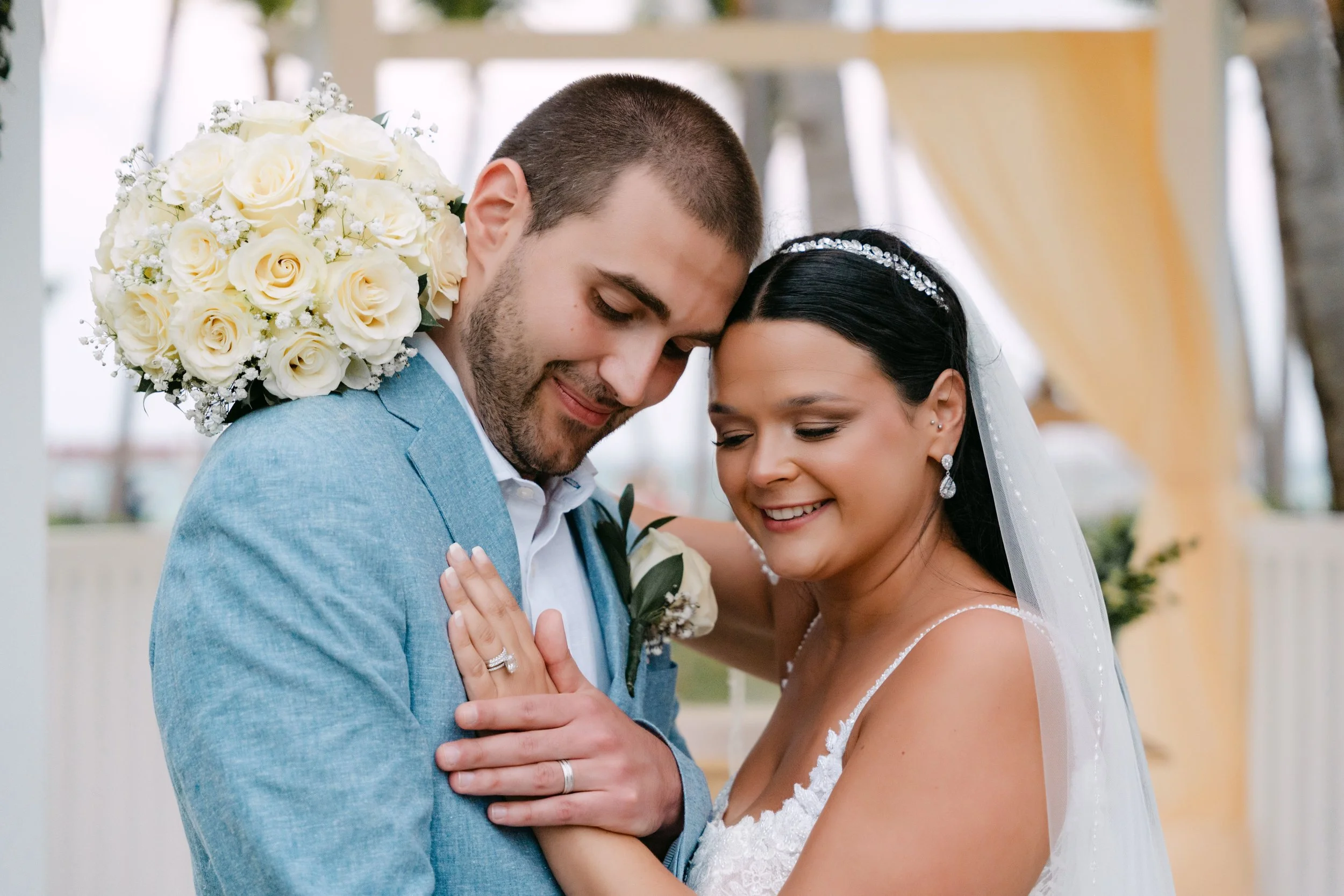 Bride and groom in a close embrace with bouquet between them under the gazebo at Dreams Flora